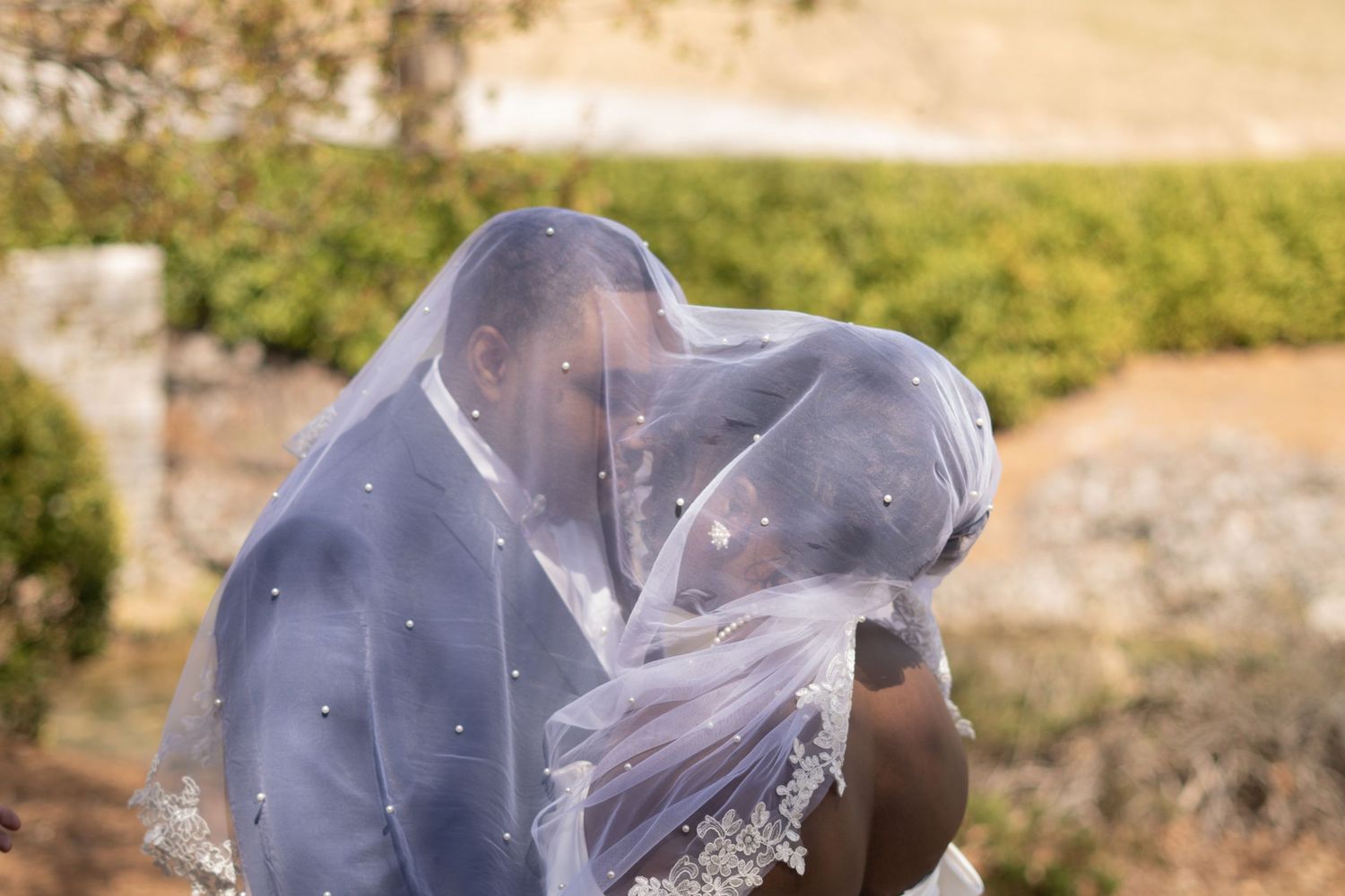 A romantic moment between newlyweds under a flowing veil against natural scenery.
