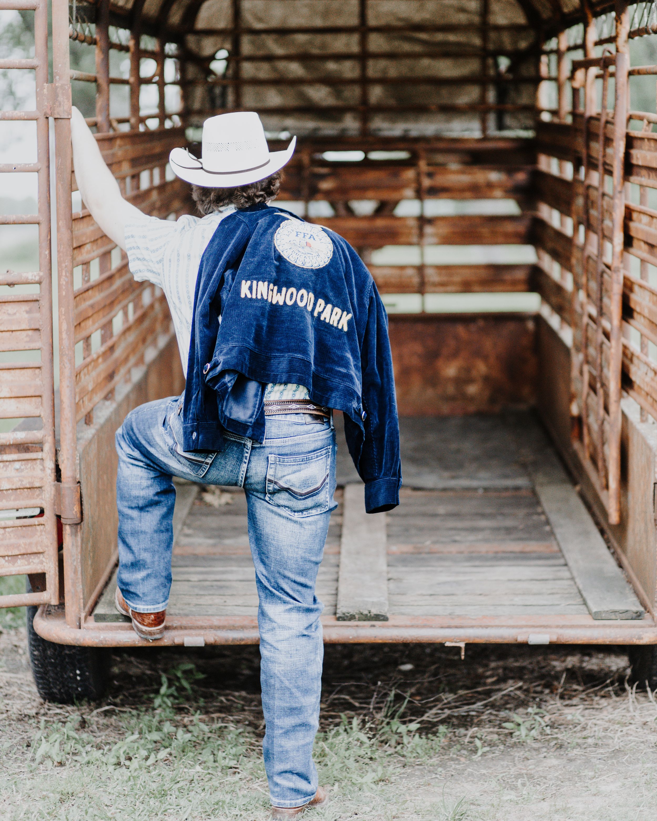 A person wearing a blue jacket and cowboy hat stands in a wooden livestock chute on a ranch.