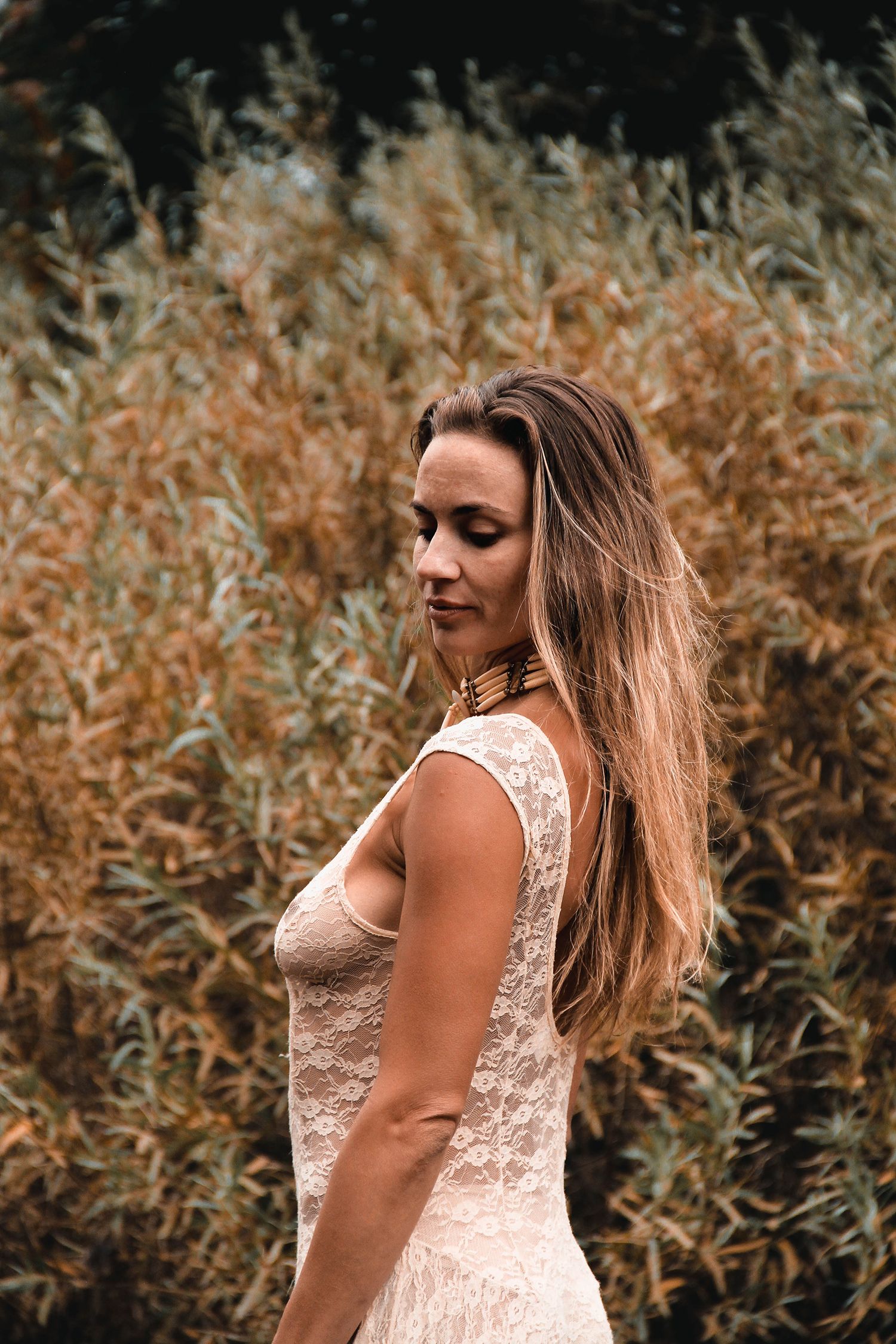 A person in a sleeveless lace dress poses against autumn foliage on a moody fall day.