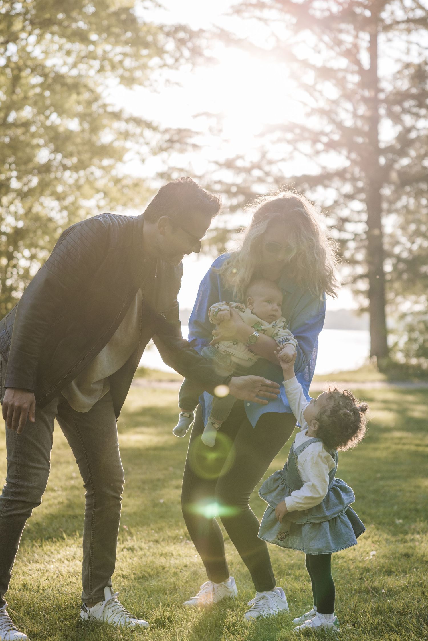 Family bending down together in a sunlit park during golden hour.