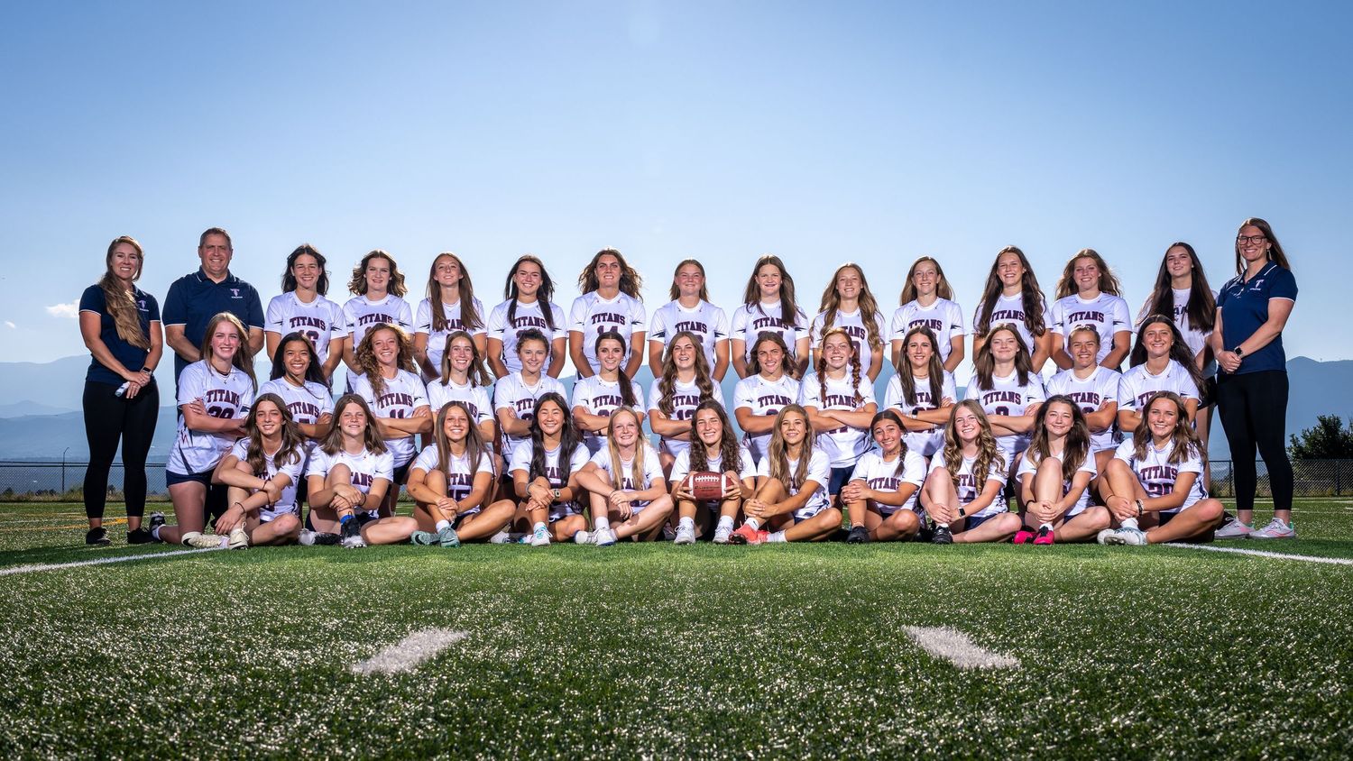 High school sports team and coaches pose for official team photo on field.