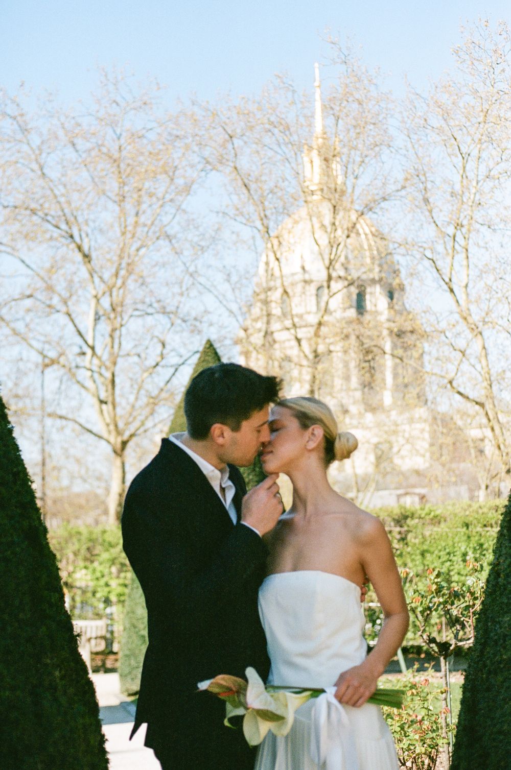 A romantic moment in front of Les Invalides church in Paris with its golden dome visible through bare winter trees.