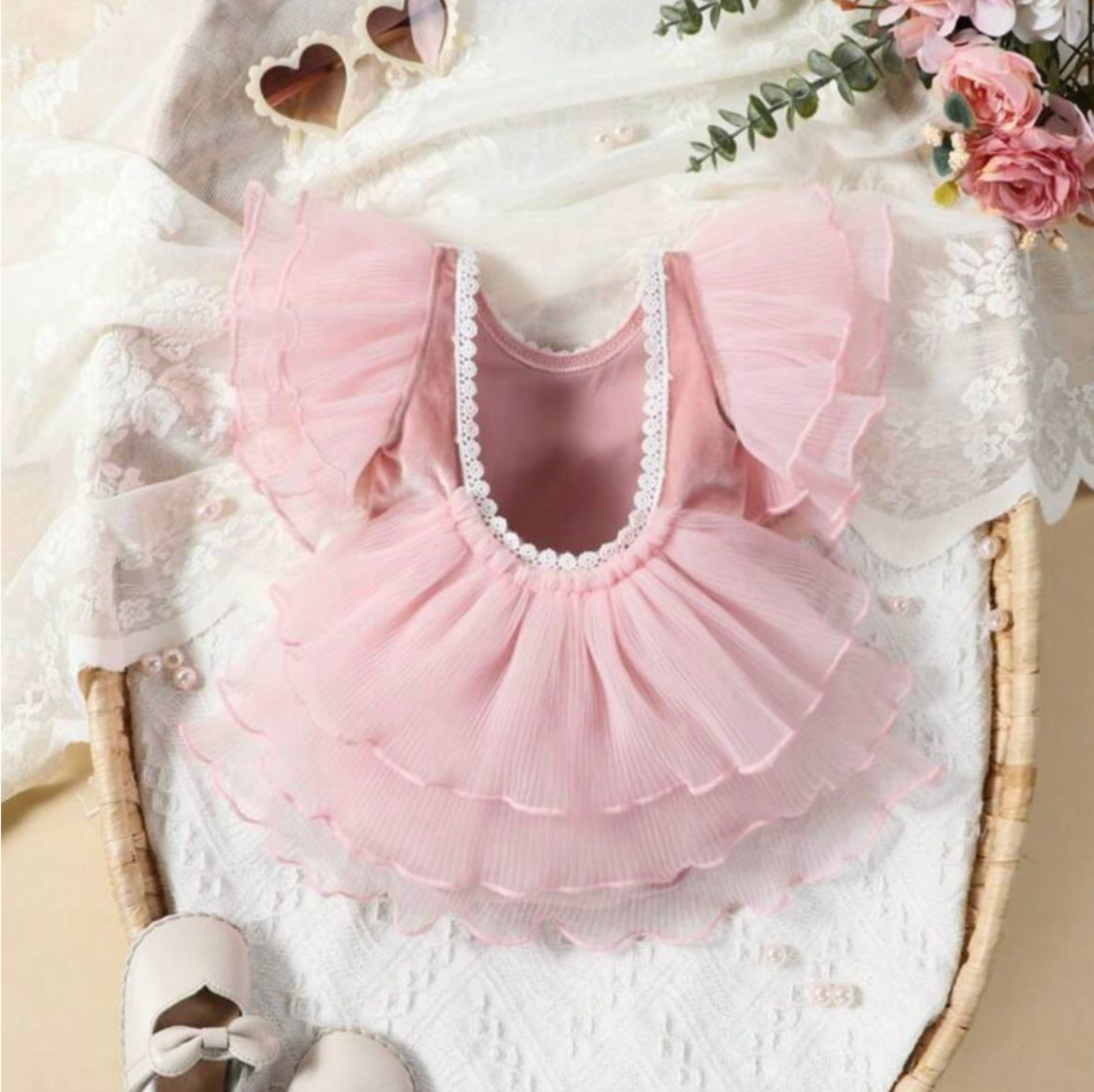 Delicate pink tulle baby dress with ruffles and pearls laid flat on white surface.
