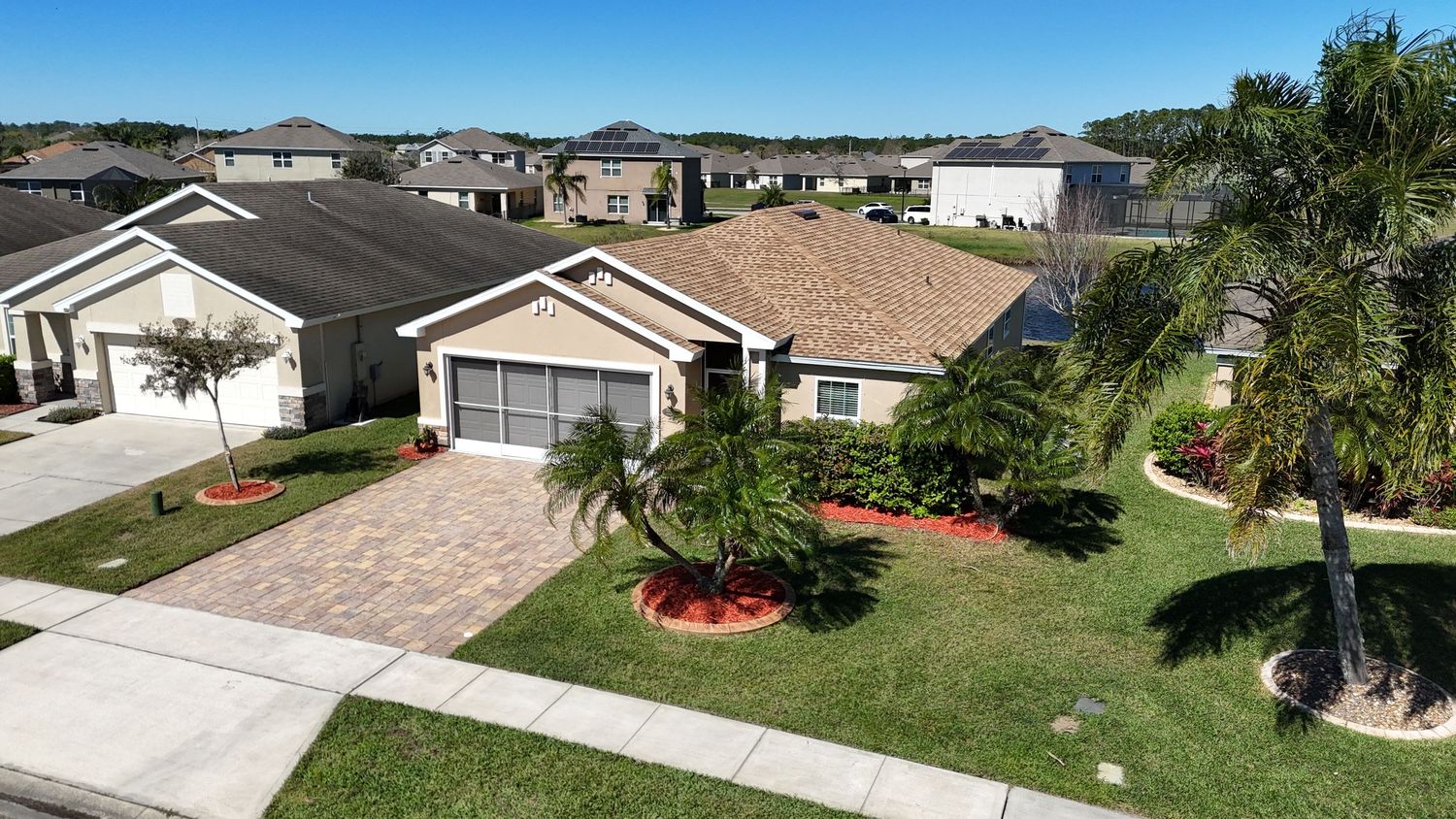 Modern Florida-style home with palm trees and red mulch landscaping viewed from above.