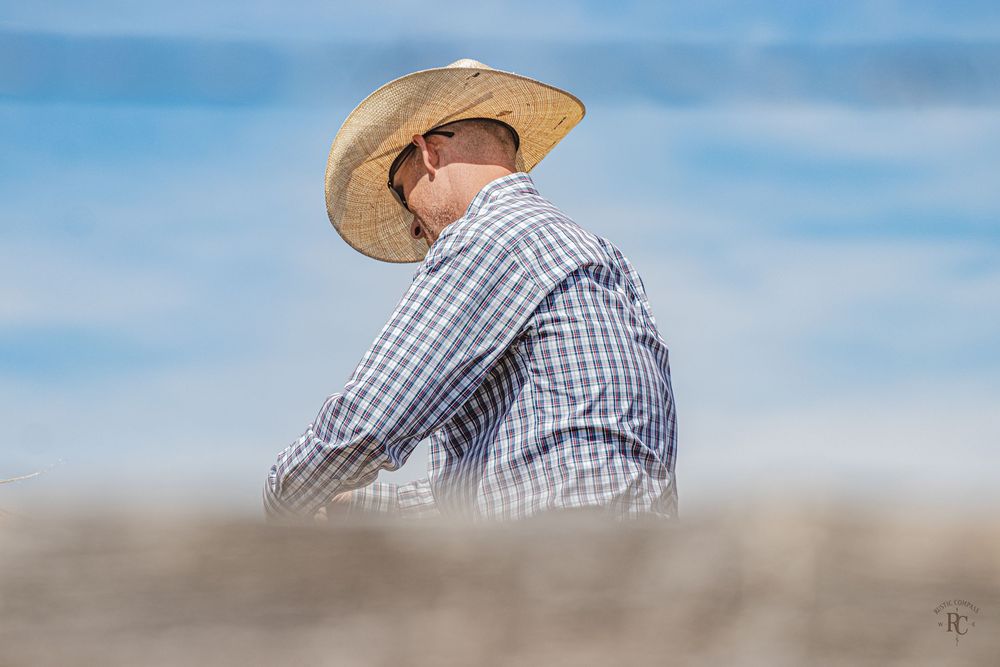 Cowboy behind a rustic wooden fence in a straw cowboy hat with a beautiful blue sky background