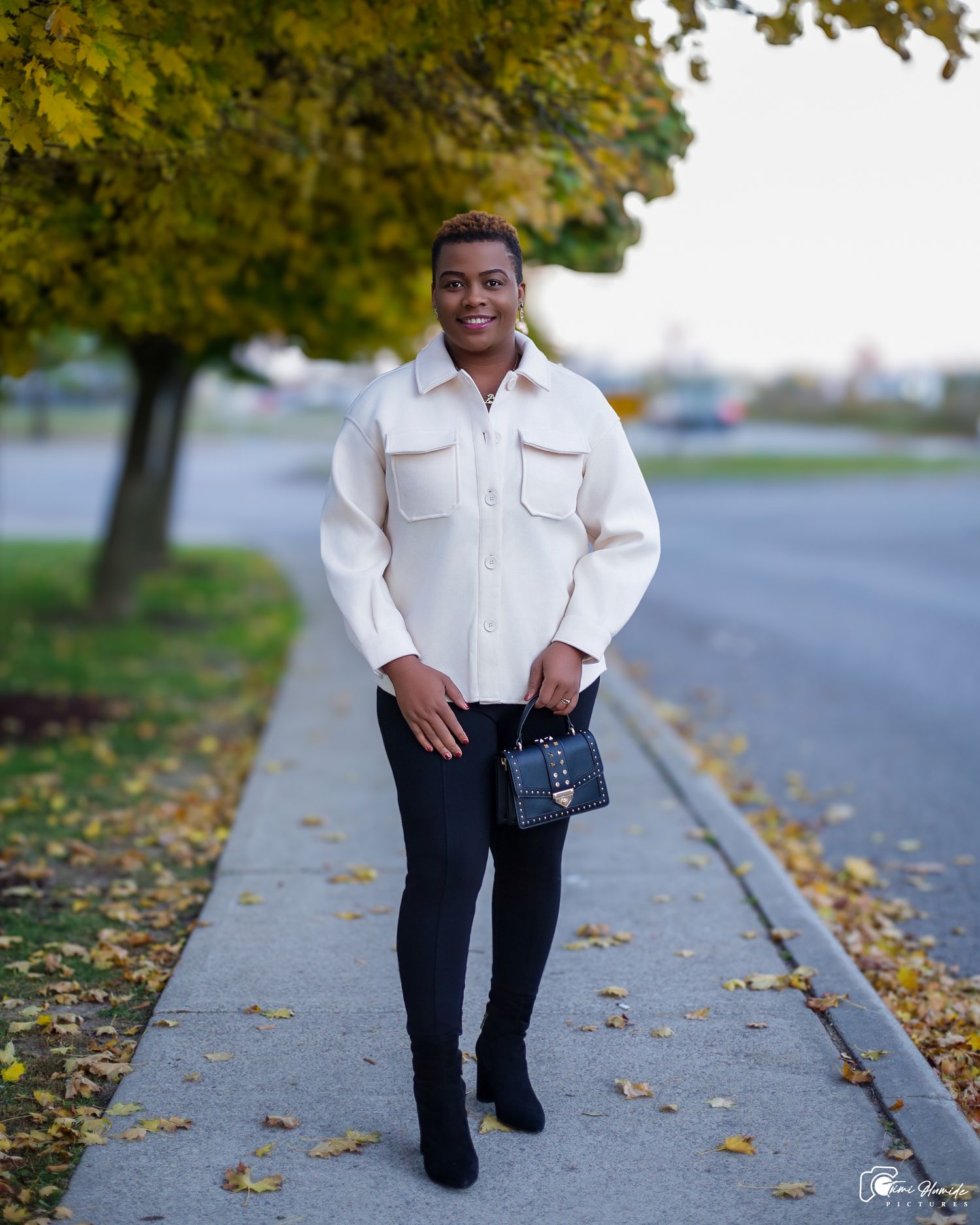 Casual autumn portrait of someone in white sweater and dark pants walking on leaf-covered sidewalk.