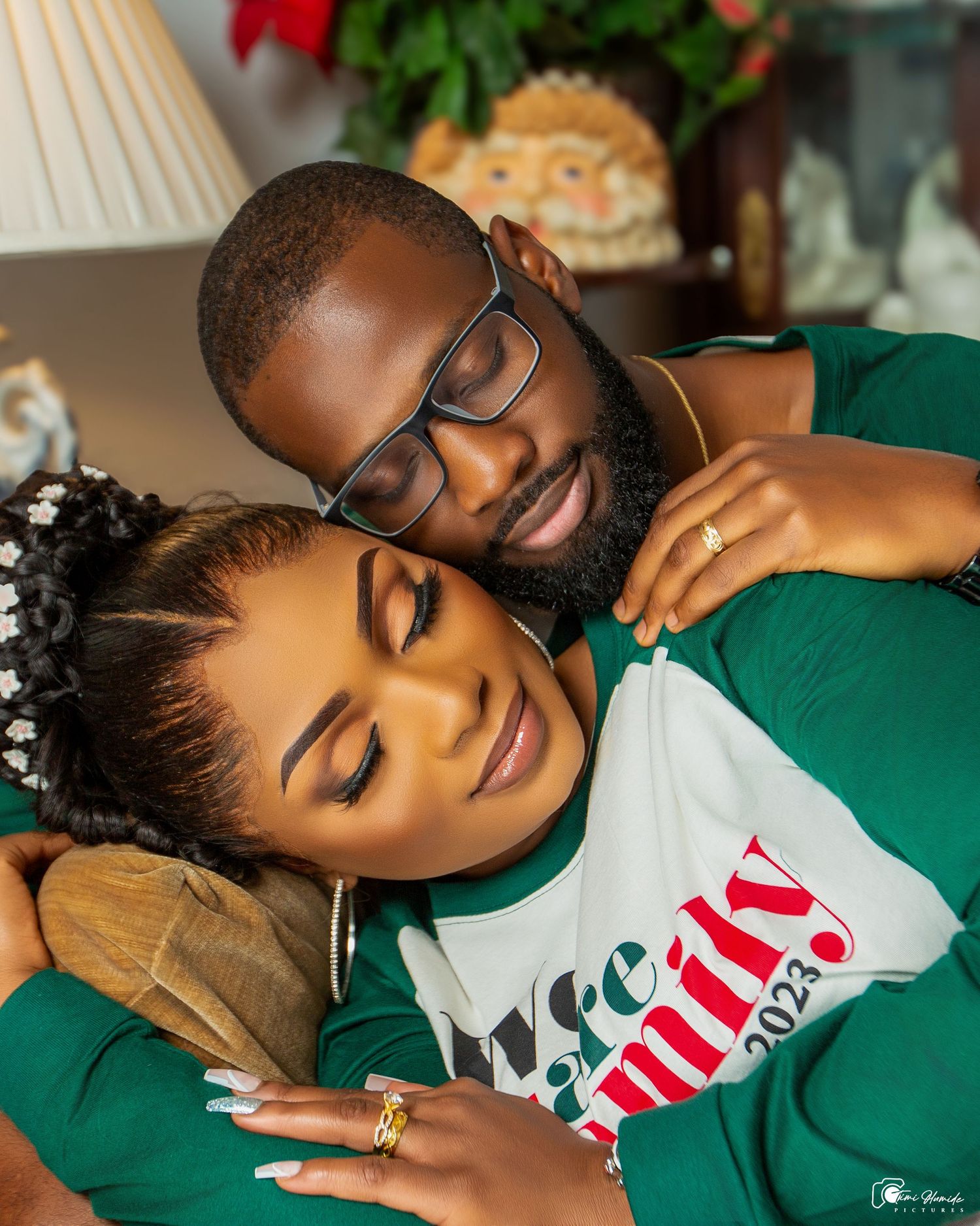 Intimate holiday portrait of couple in green and white outfits cuddling on couch with Christmas decor.