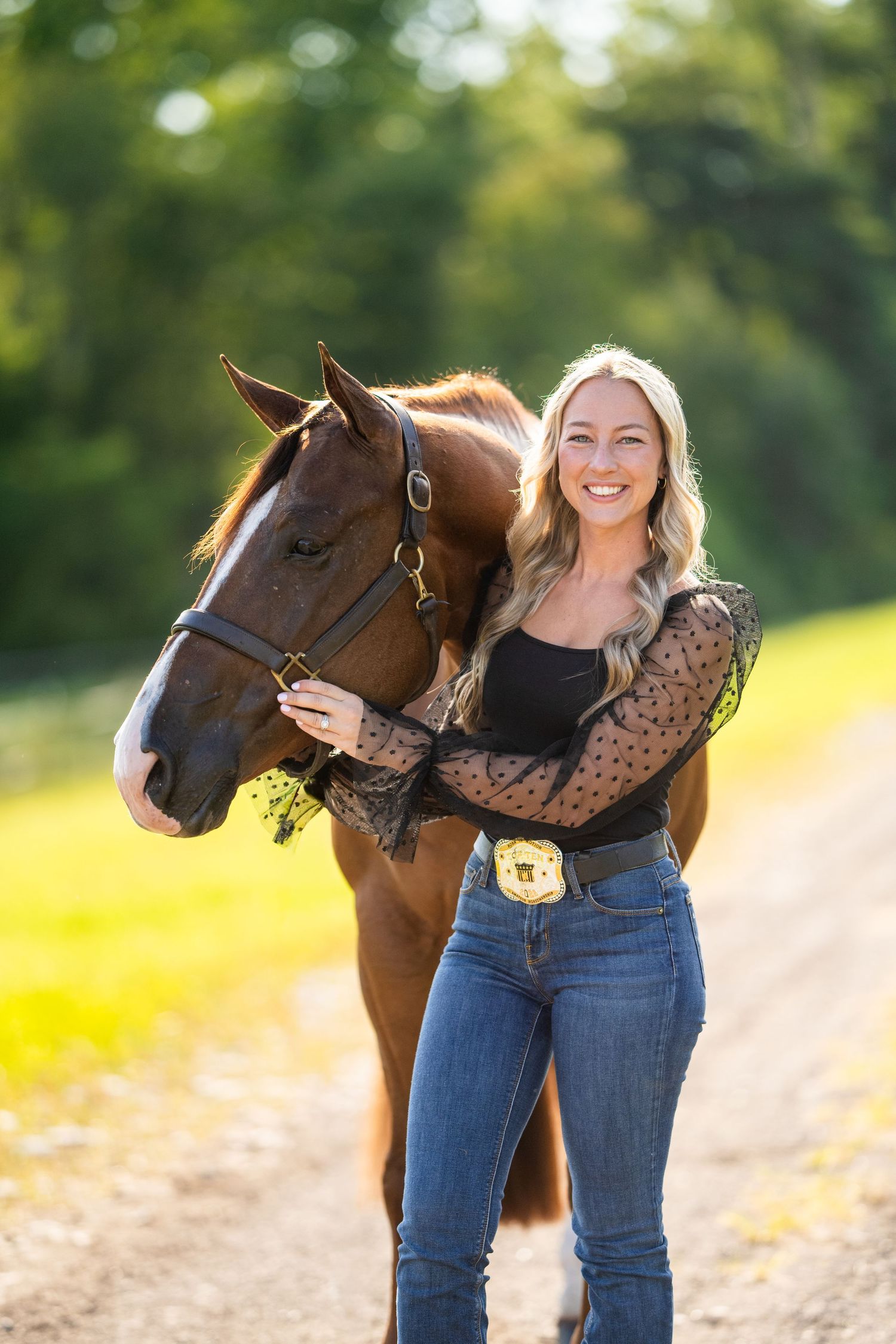 Brown horse and handler in casual denim and lace posing on dirt path during sunset.
