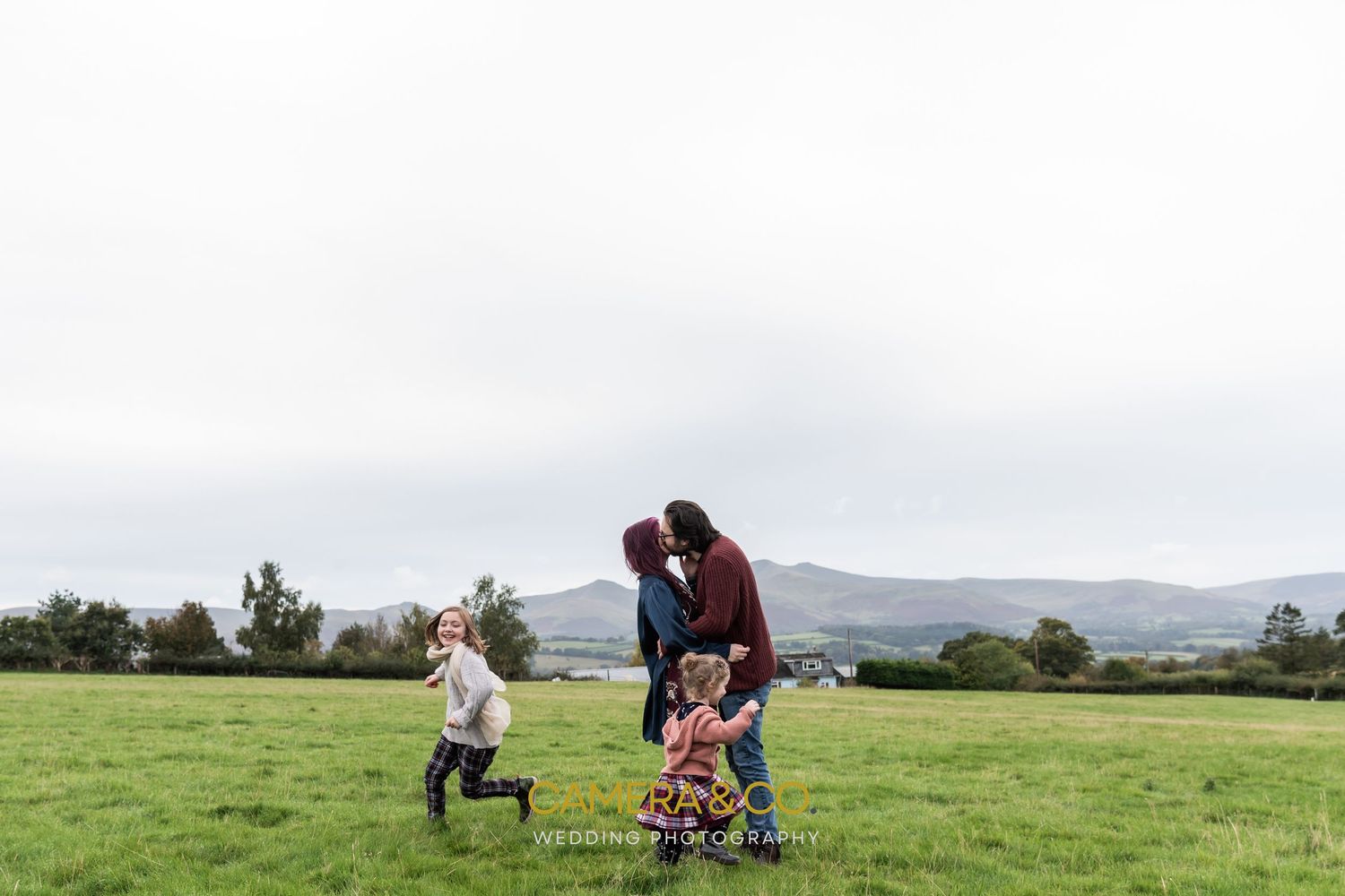 Candid outdoor family photography session in a green field with mountains in background.