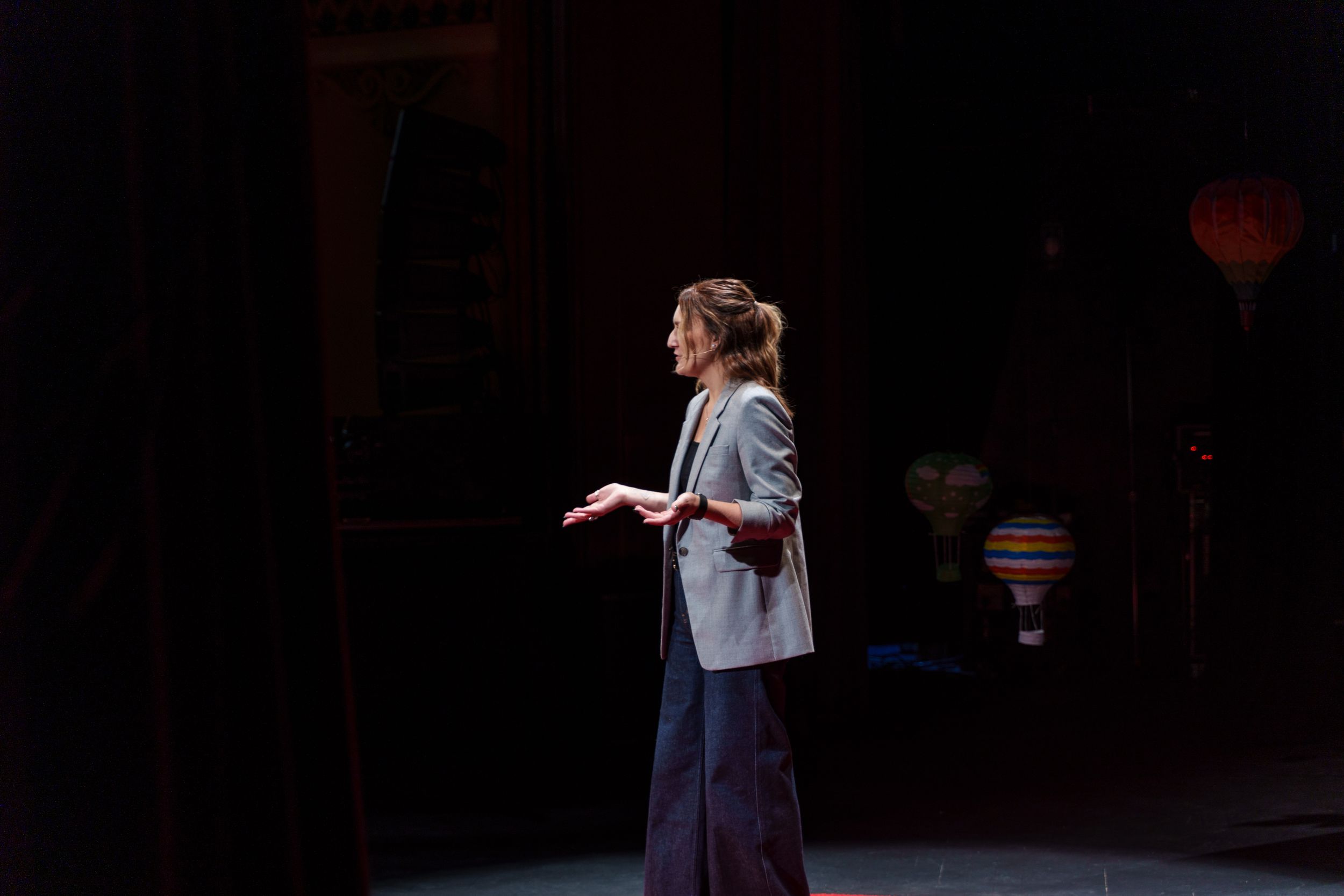 A presenter speaks on a darkened stage with spotlights and hot air balloon decorations.