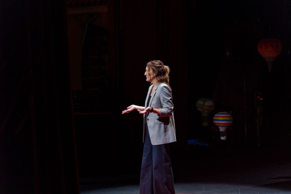 A presenter speaks on a darkened stage with spotlights and hot air balloon decorations.