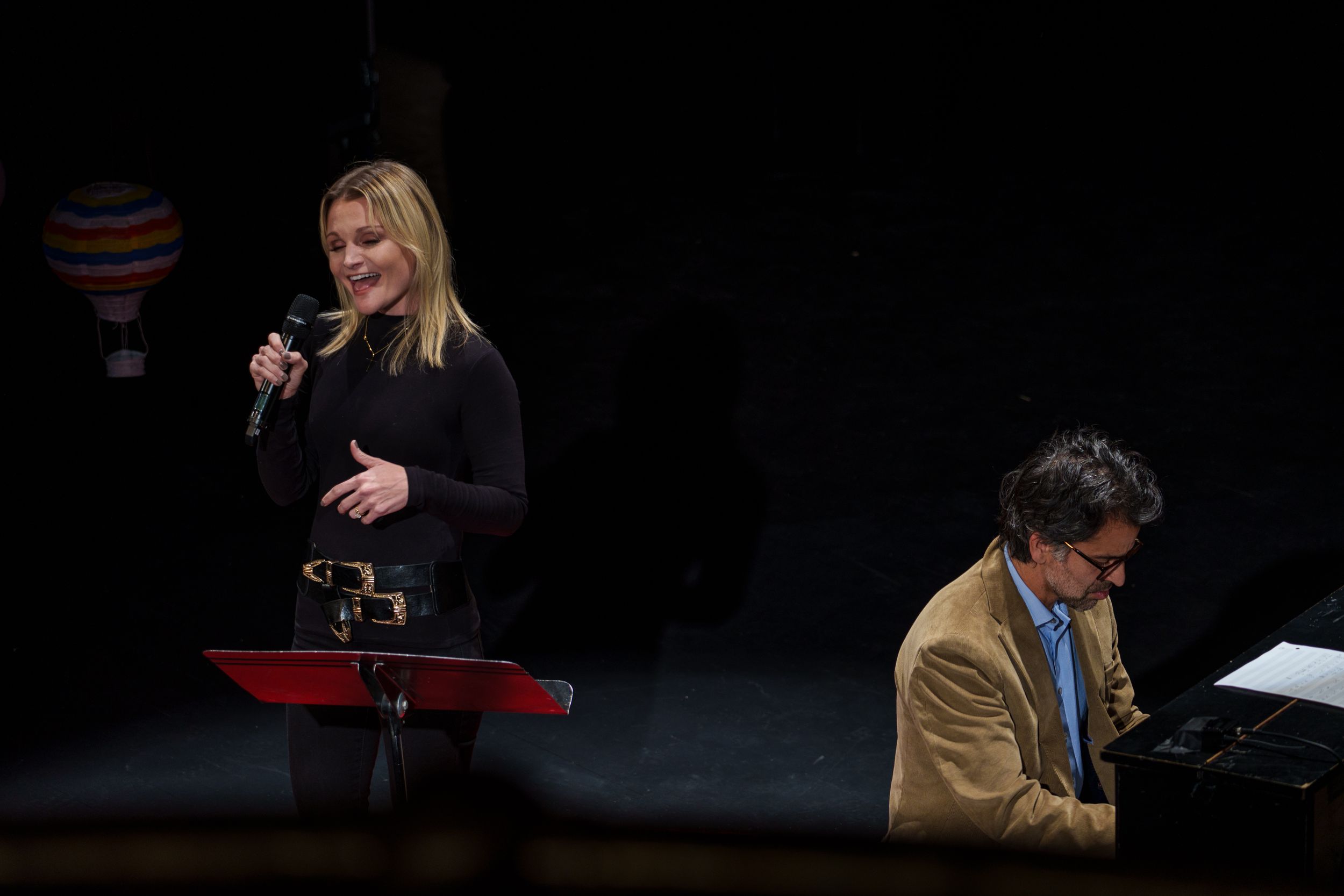 A performance featuring a singer and pianist on a dark stage with minimal lighting.