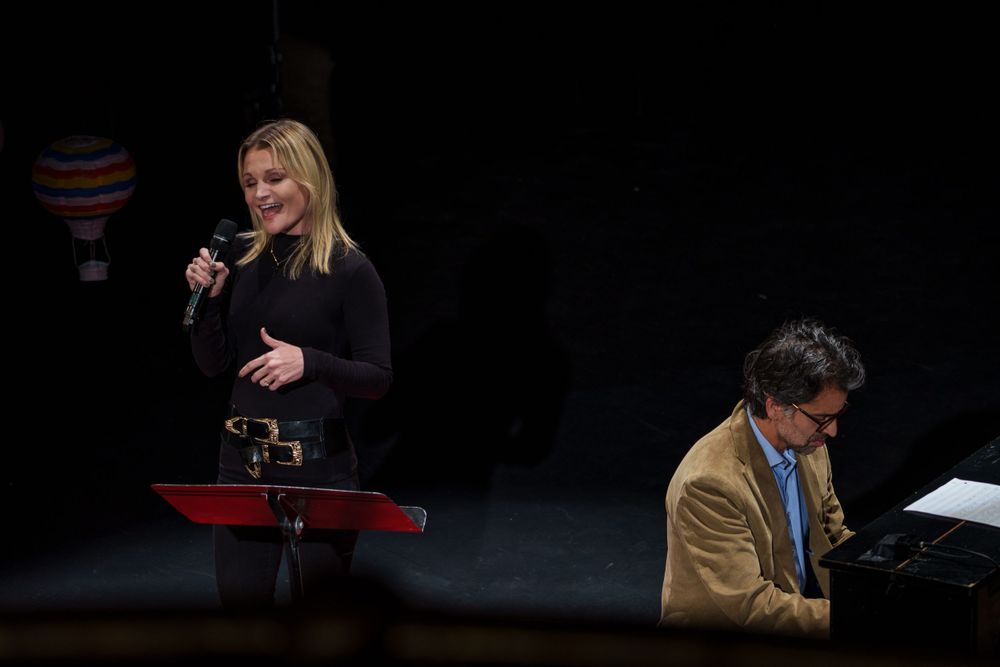 A performance featuring a singer and pianist on a dark stage with minimal lighting.
