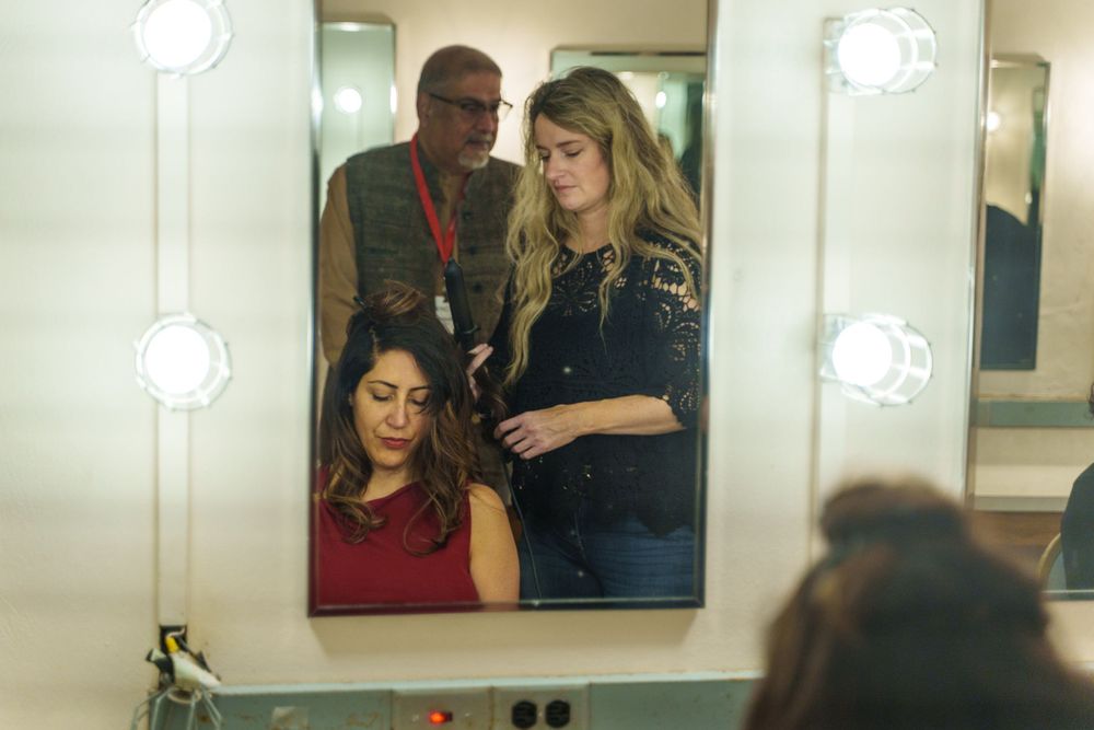 Mirror reflection showing backstage preparations with makeup and styling.