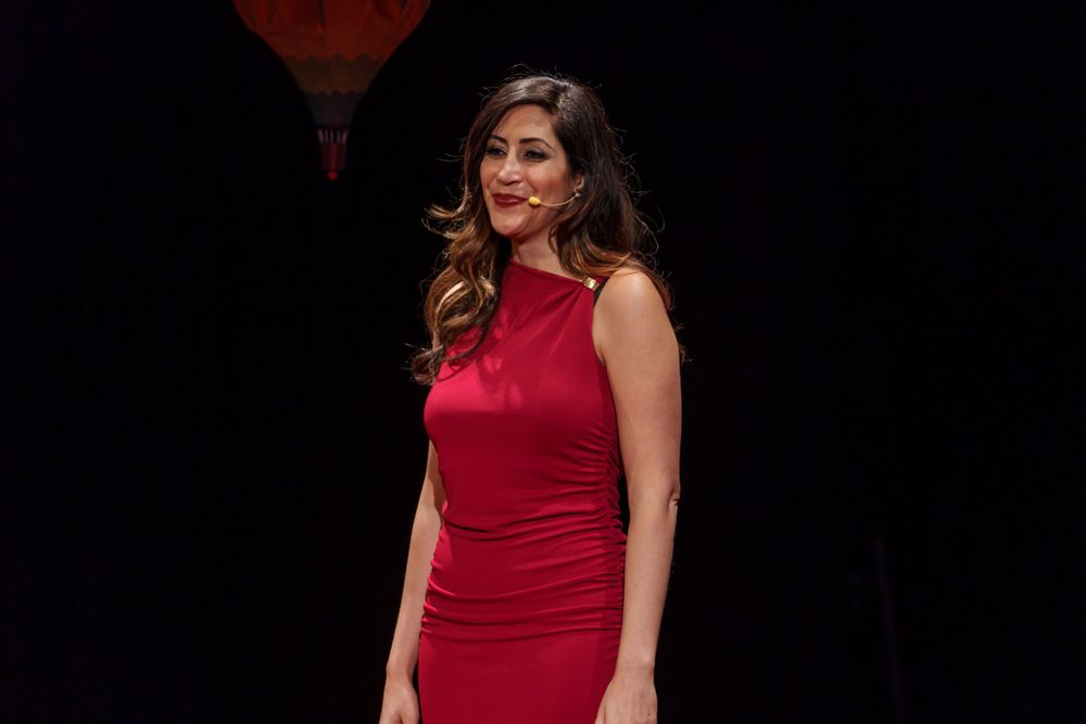 A presenter in a red dress stands on stage during a TEDx event.