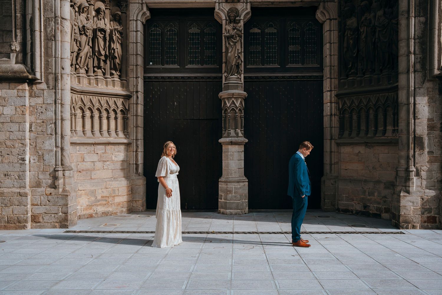 An artistic wedding portrait with couple separated by cathedral doors in dramatic composition.
