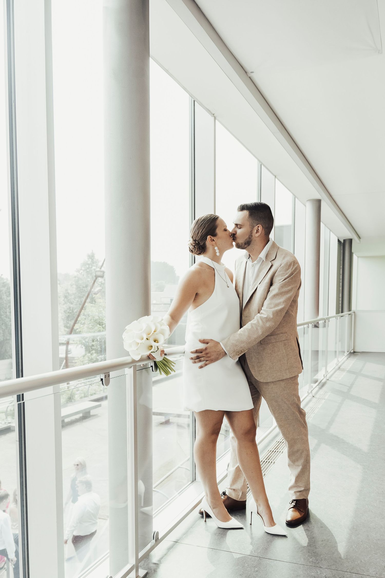 A romantic moment between newlyweds by large windows in a modern building.