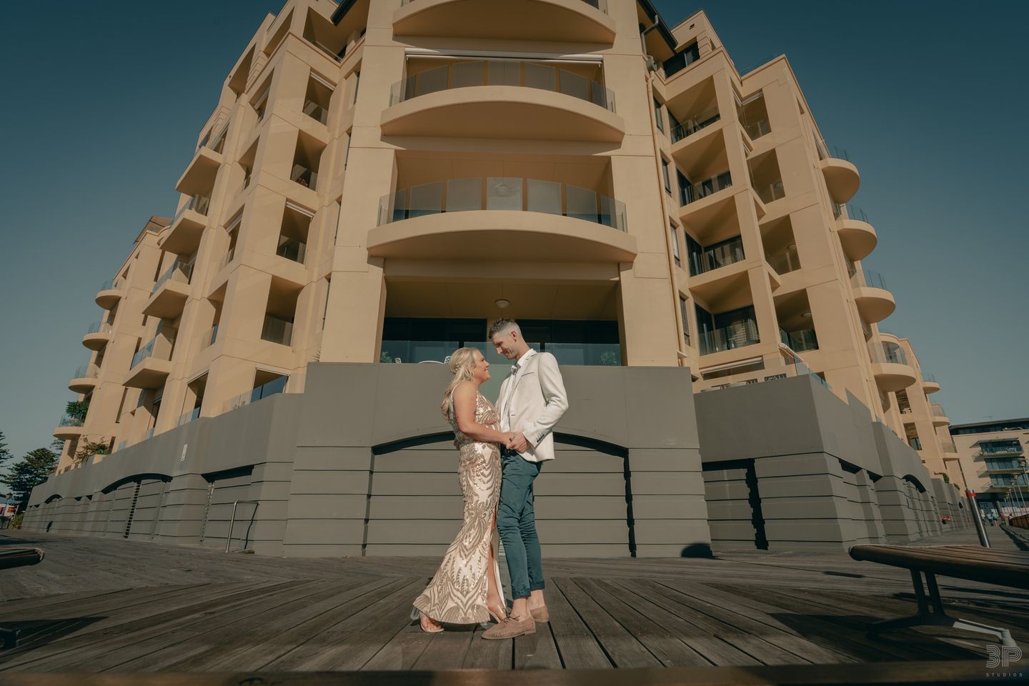 Wedding couple poses in elegant attire against modern architectural backdrop.