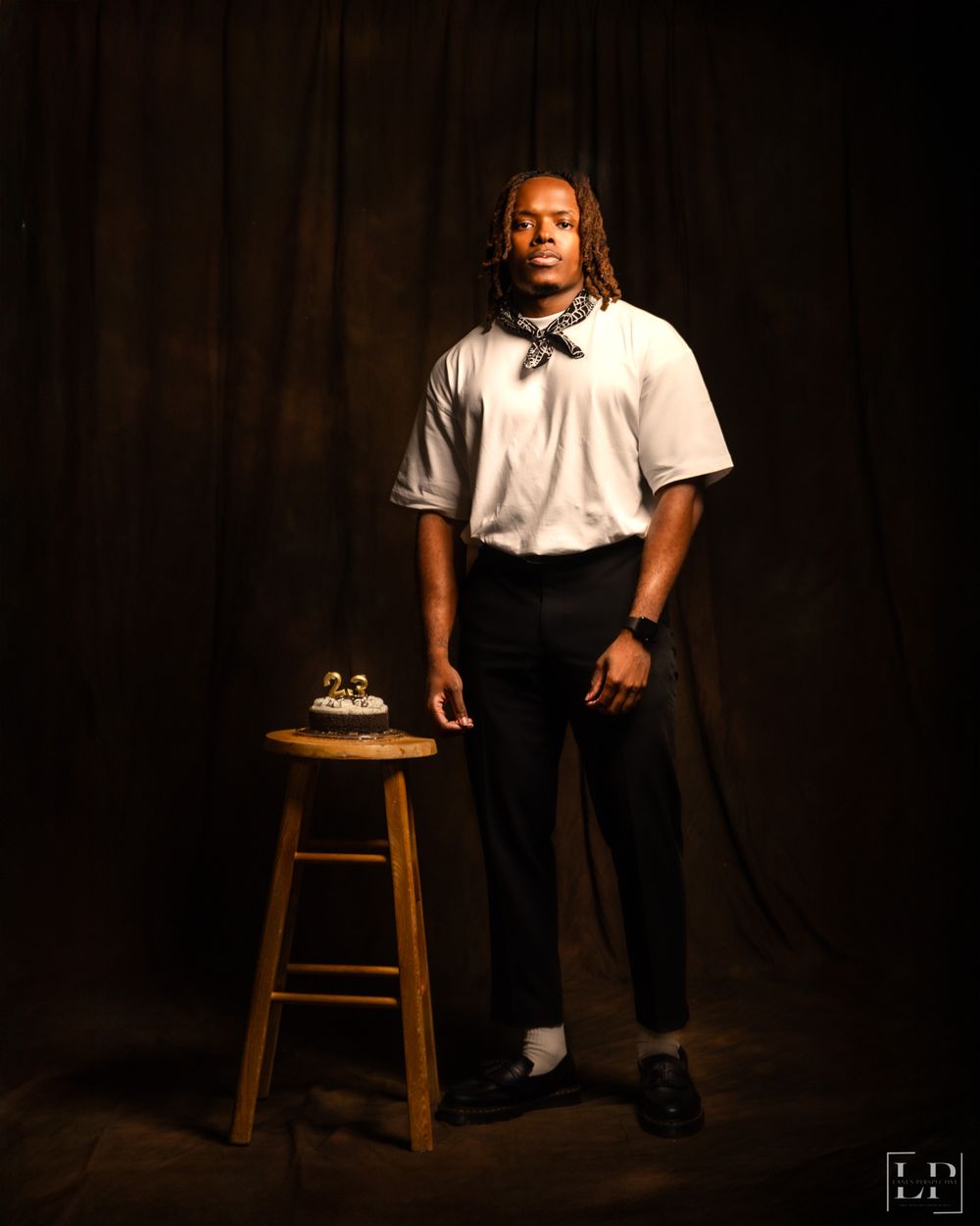Dramatic studio portrait with wooden stool against dark background.