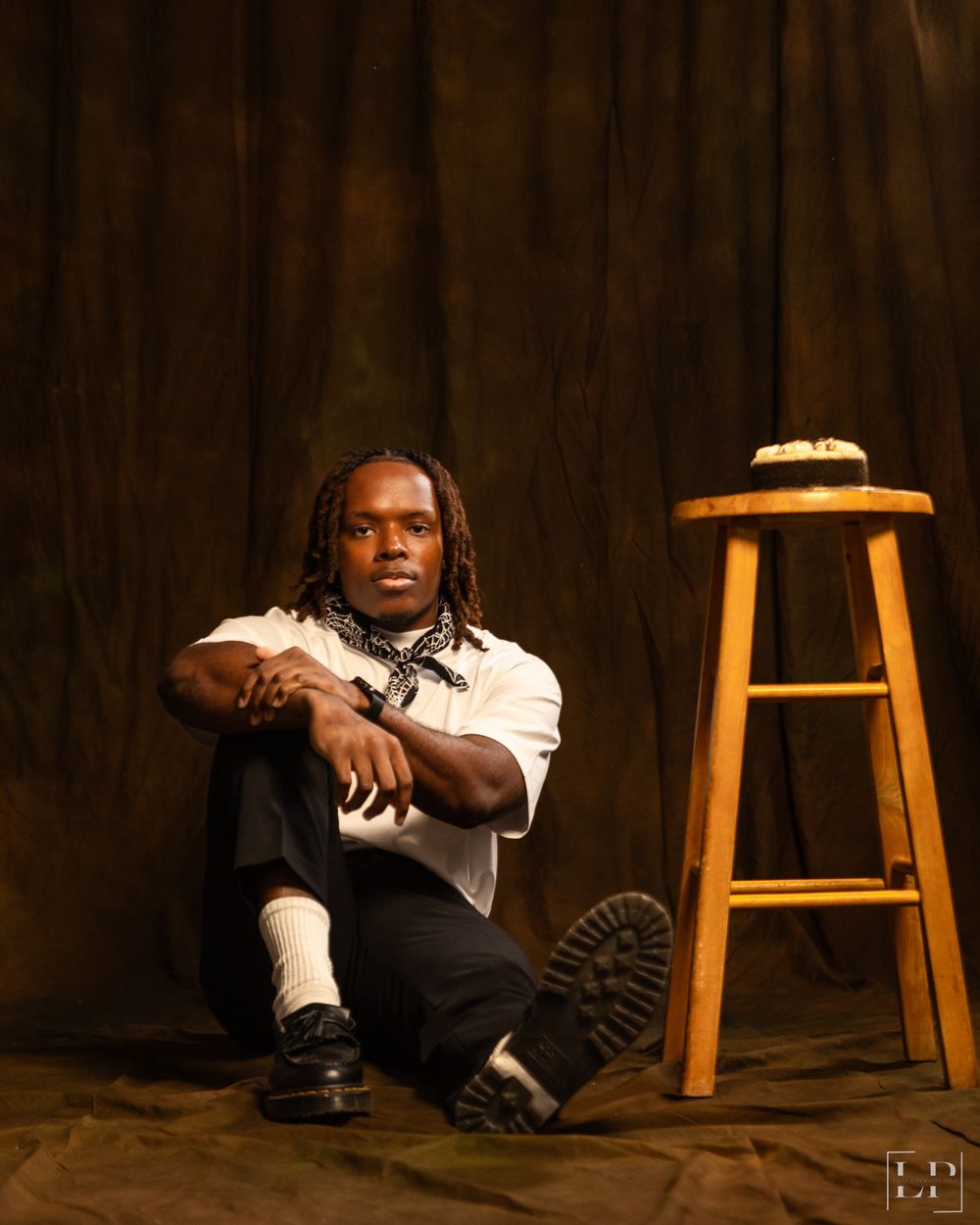 Artistic low-key portrait with wooden stool and dramatic lighting on dark background.