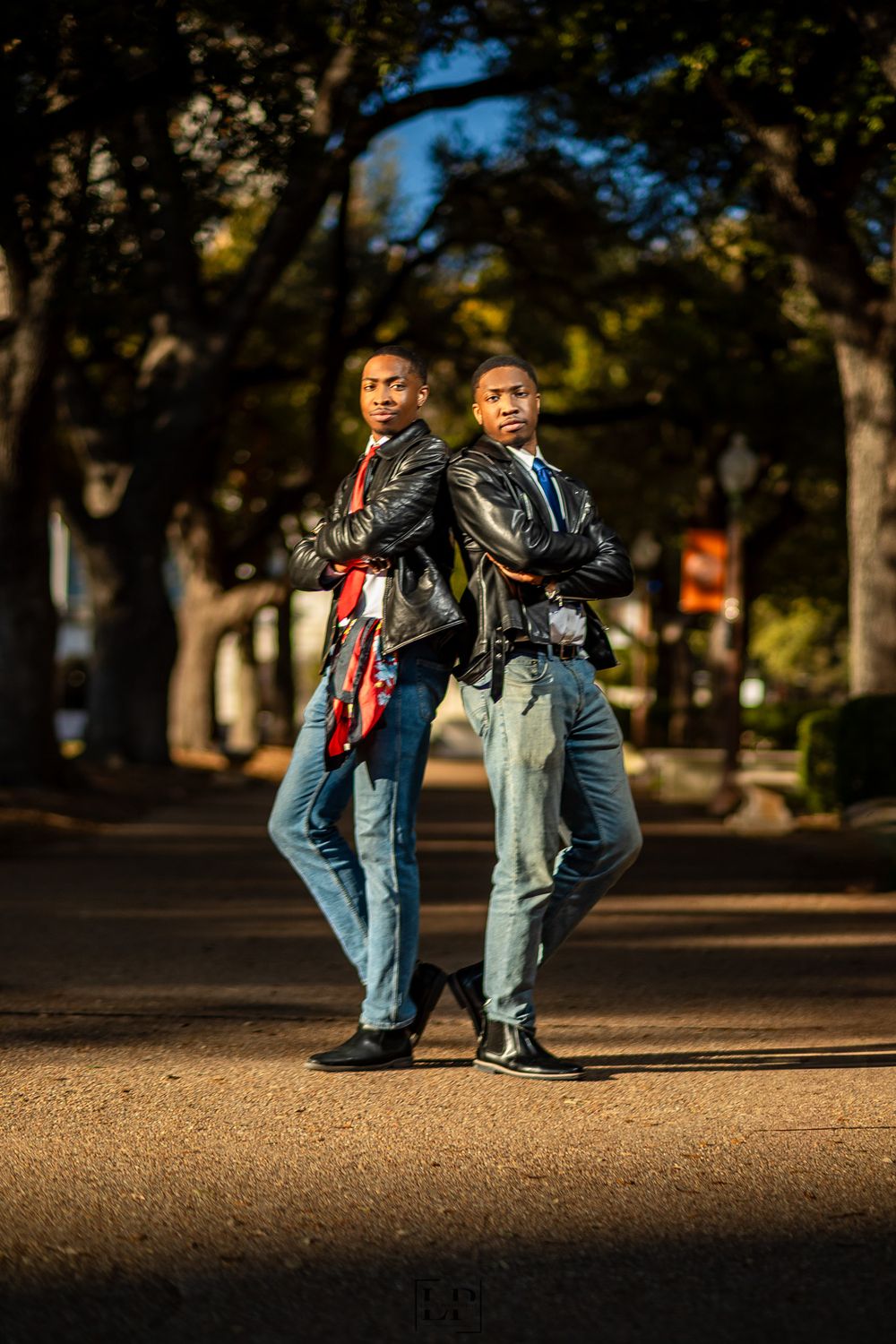 Two people in denim and leather jackets pose together on urban street at golden hour.