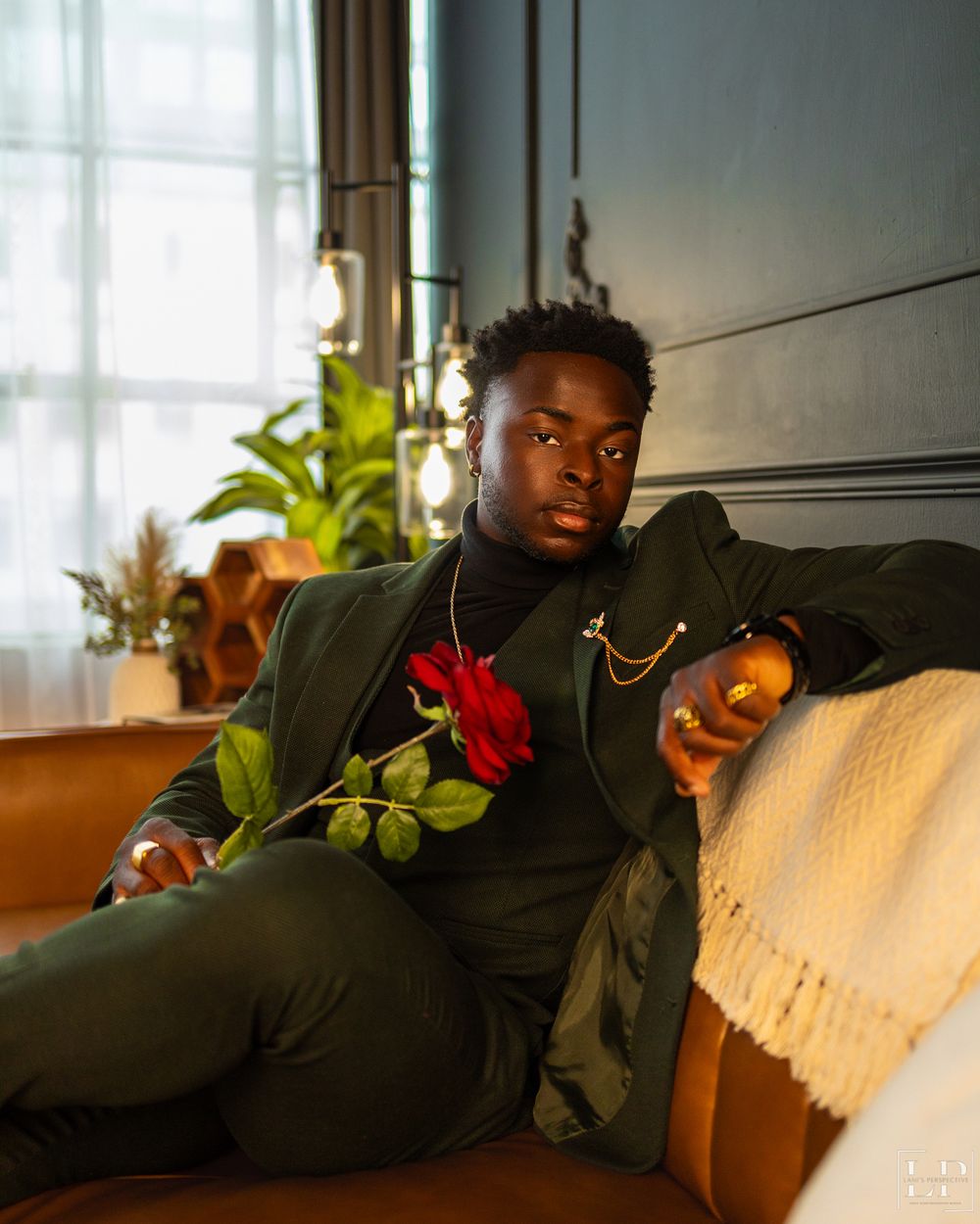 Person in dark suit reclines on couch with red flowers in elegant indoor setting.