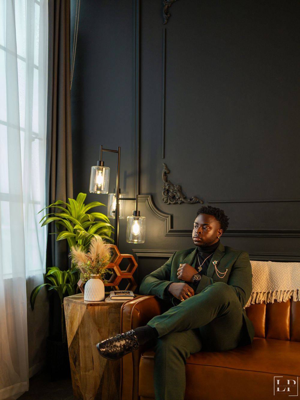 Moody interior scene with person relaxing on brown leather couch in dark room with plants.