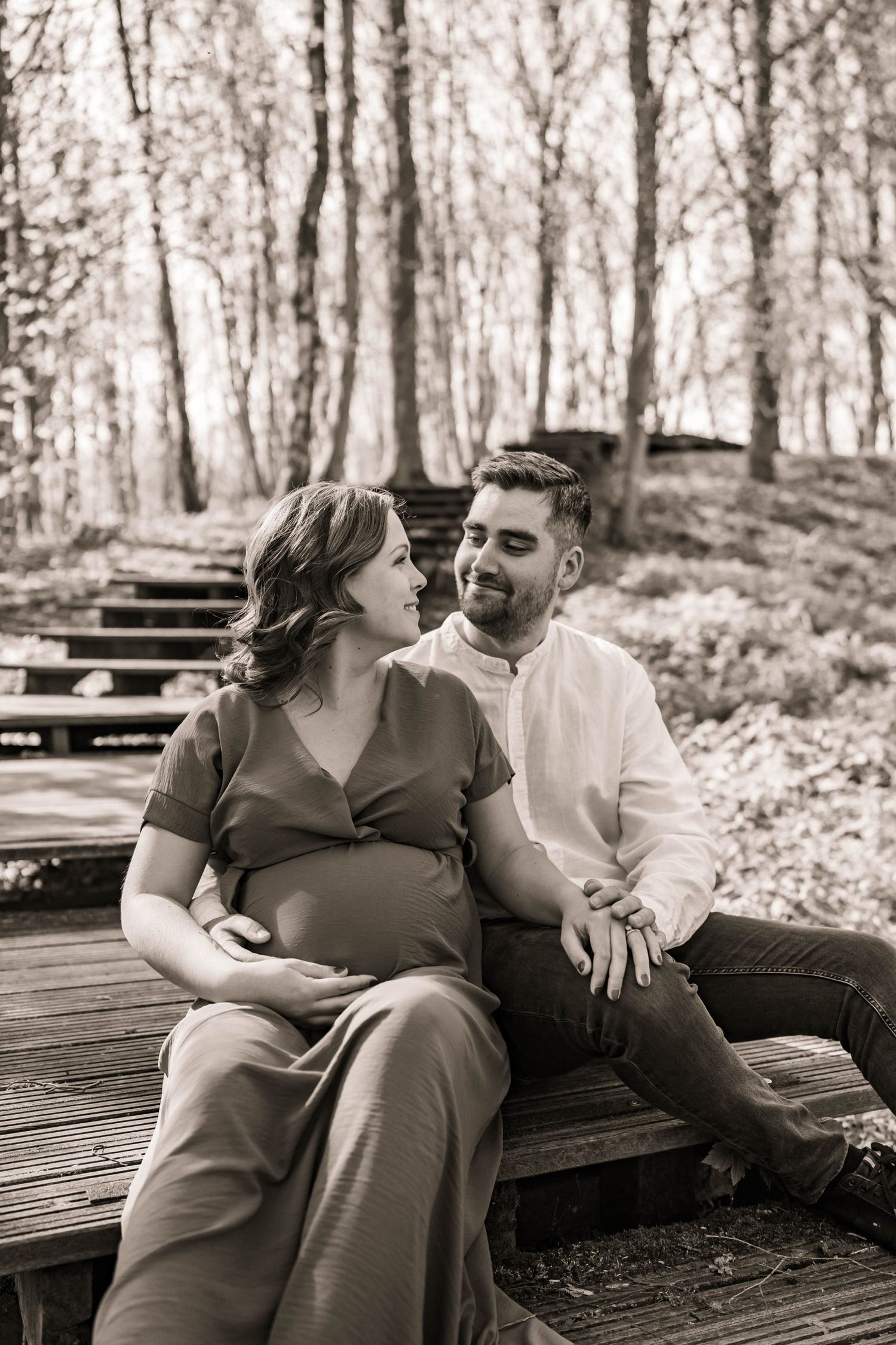 Intimate black and white portrait of an expecting couple sitting on wooden steps outdoors.