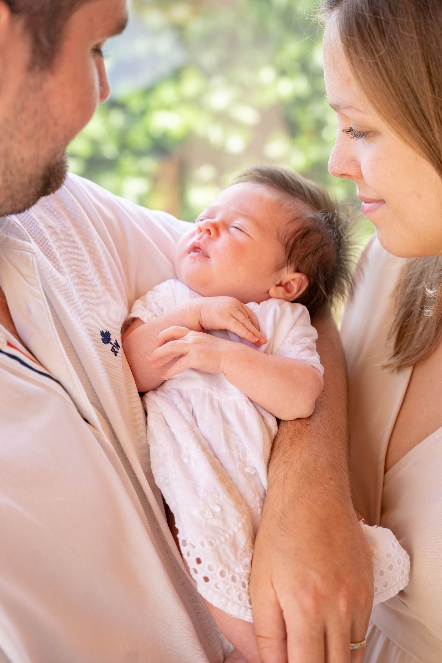 Family moment with sleeping newborn baby in white dress.