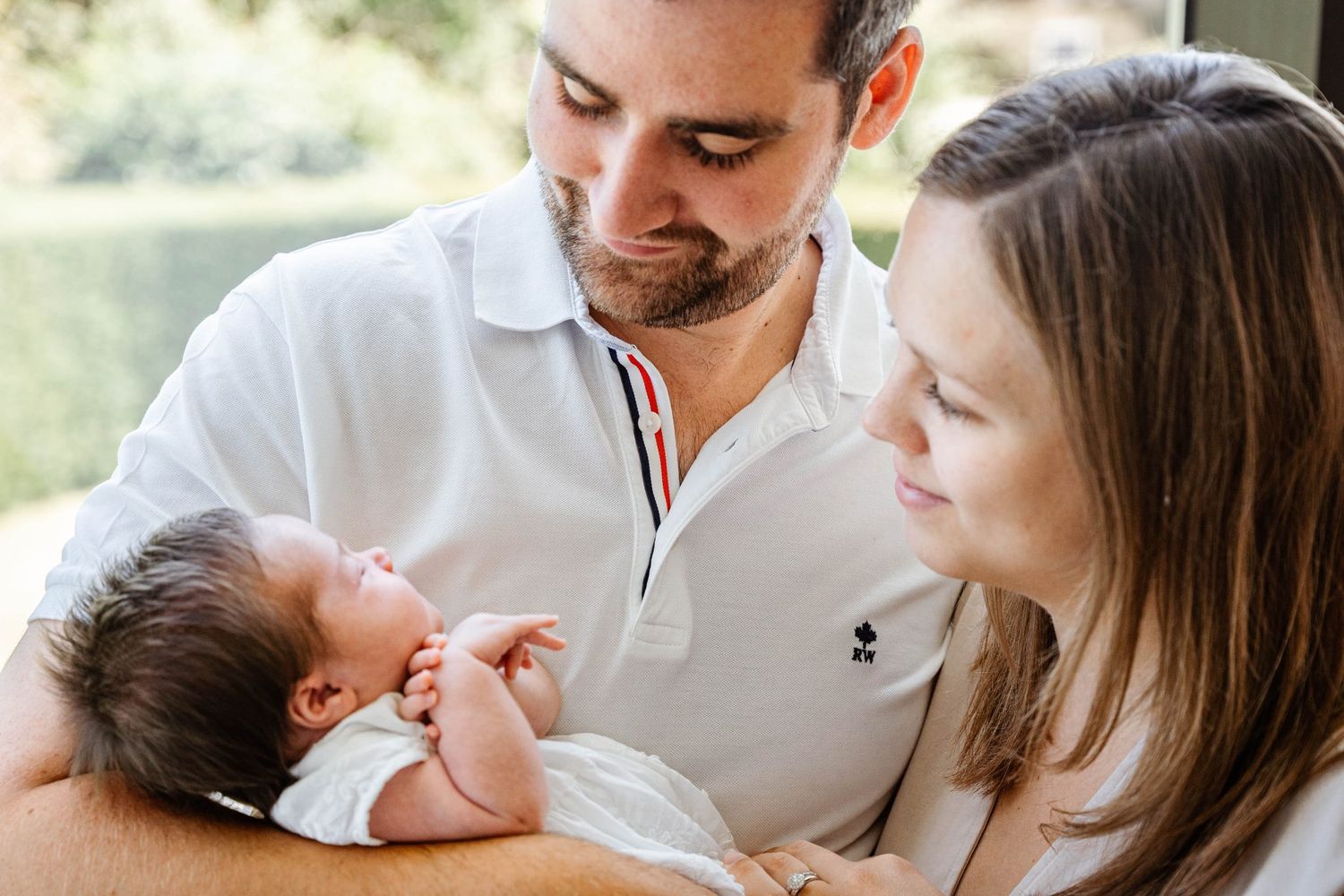 Tender family moment with newborn baby being held outdoors in natural lighting.