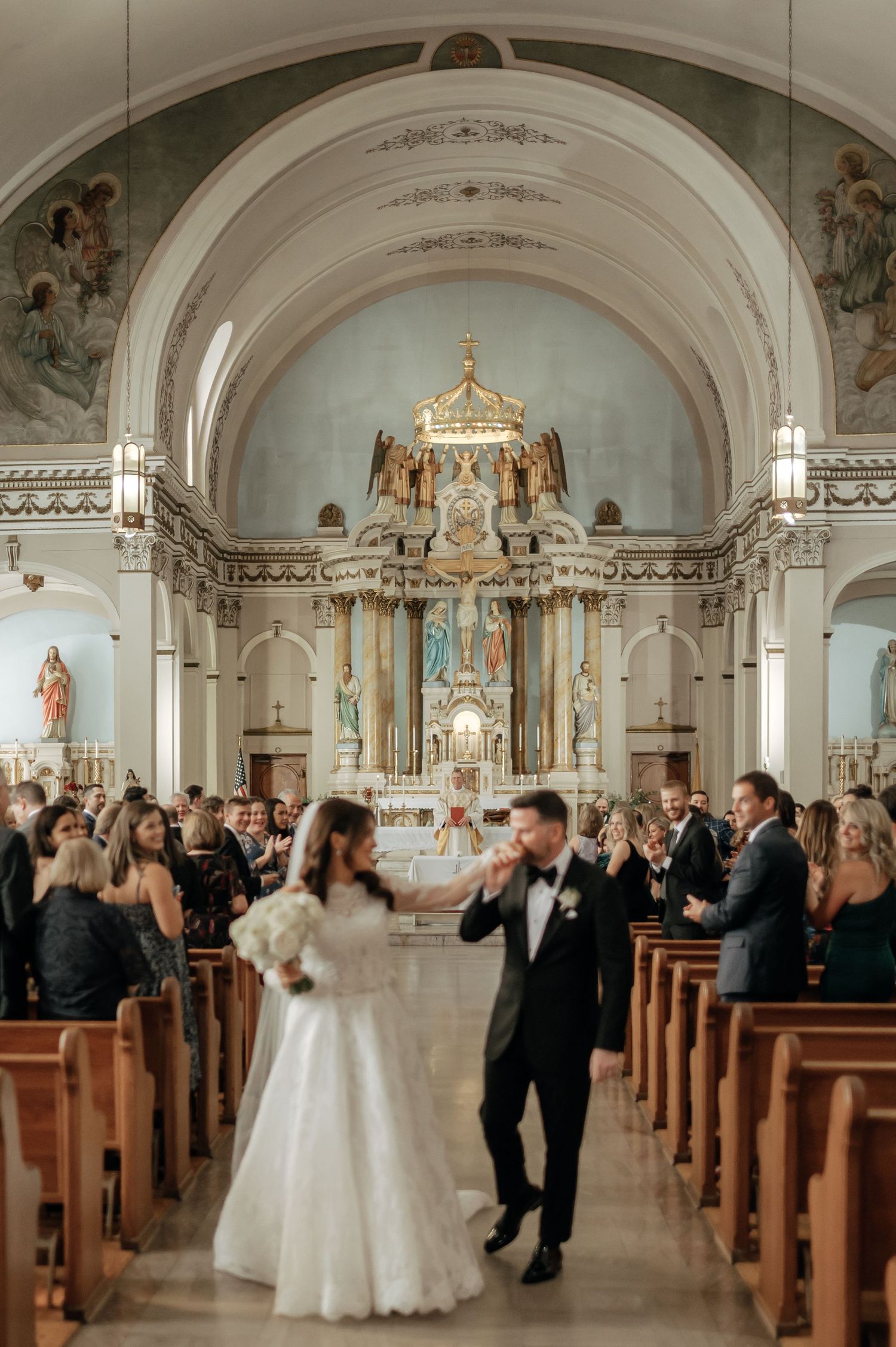 Bride and groom dancing at church altar after wedding ceremony with ornate decor and guests.