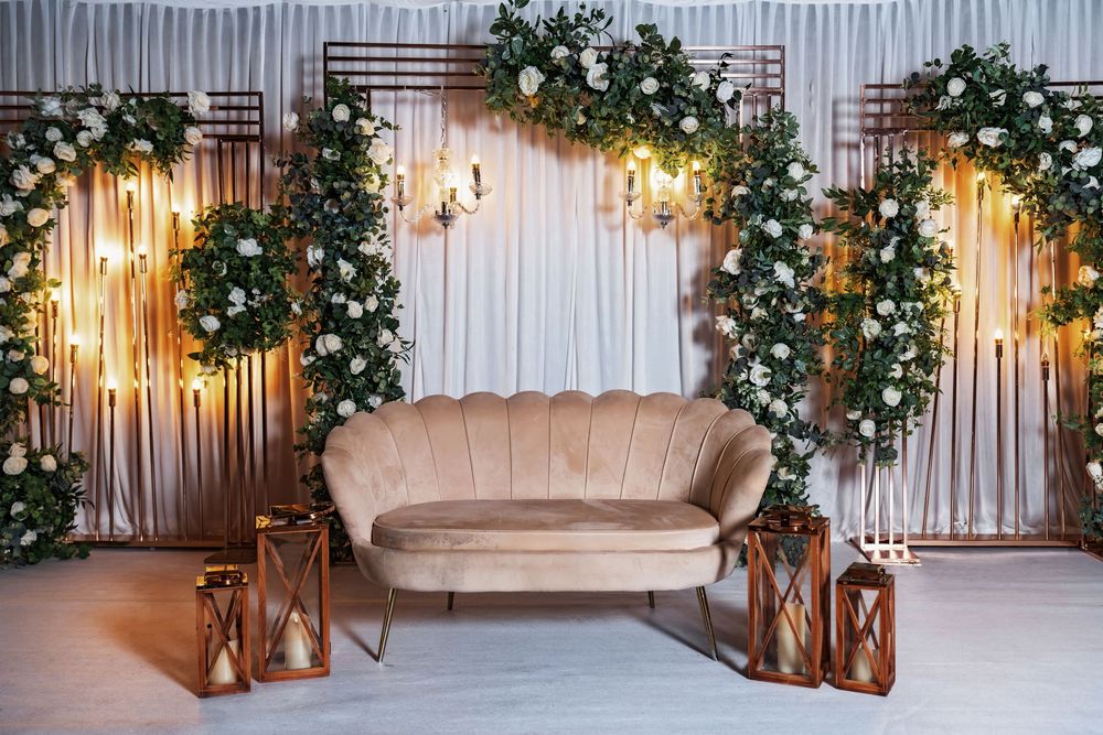 Wedding ceremony backdrop with white curtains, wooden arch, greenery garlands, and warm glowing string lights creates an elegant setting.