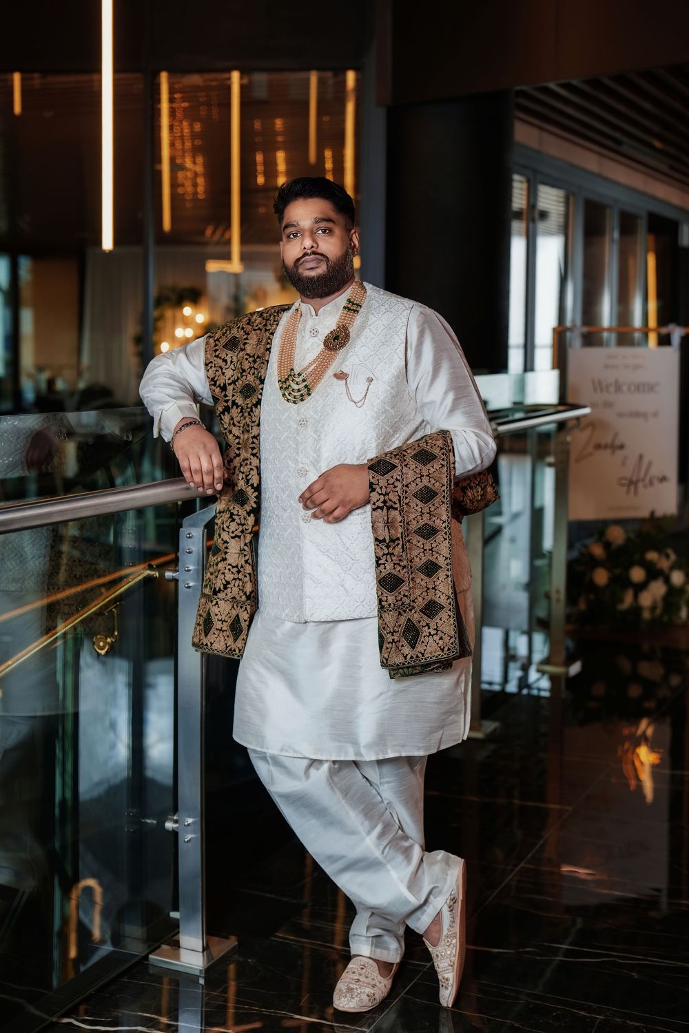 Fashion portrait of person wearing white traditional outfit and ornate patterned vest in elegant indoor setting.