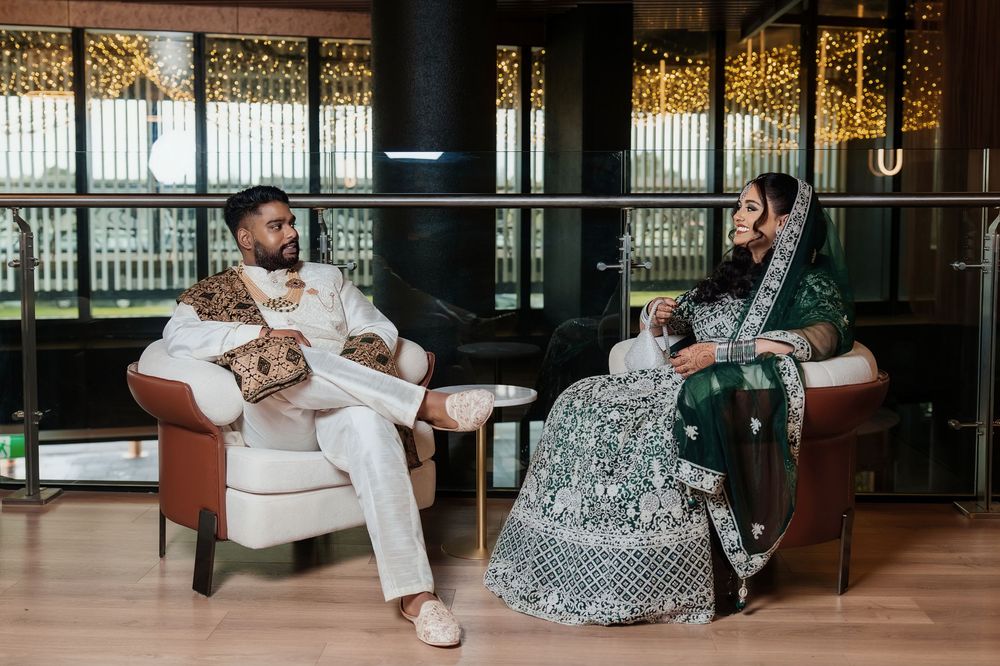 A couple in elegant attire poses together in a modern indoor venue with large windows and metal railings.