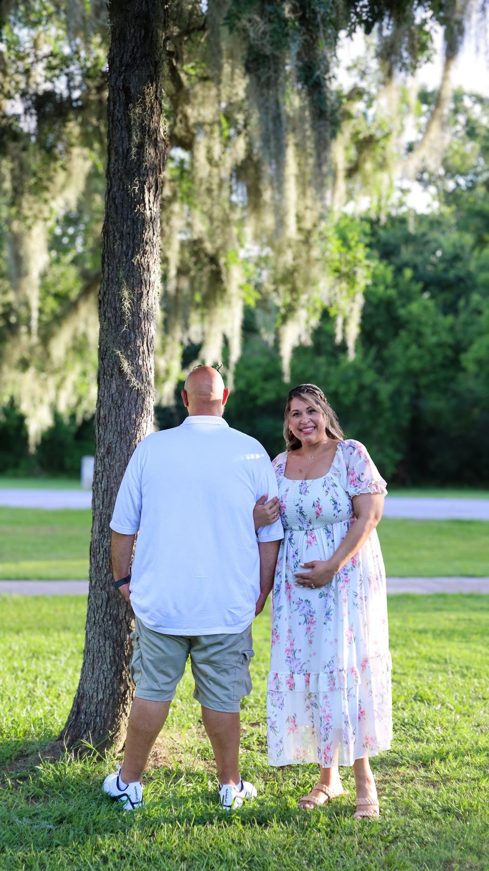 Couple walks together on grass with Spanish moss draped trees in background.