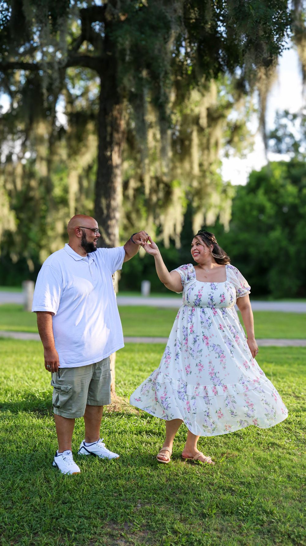 A couple dances together on grass with Spanish moss hanging from trees in the background.