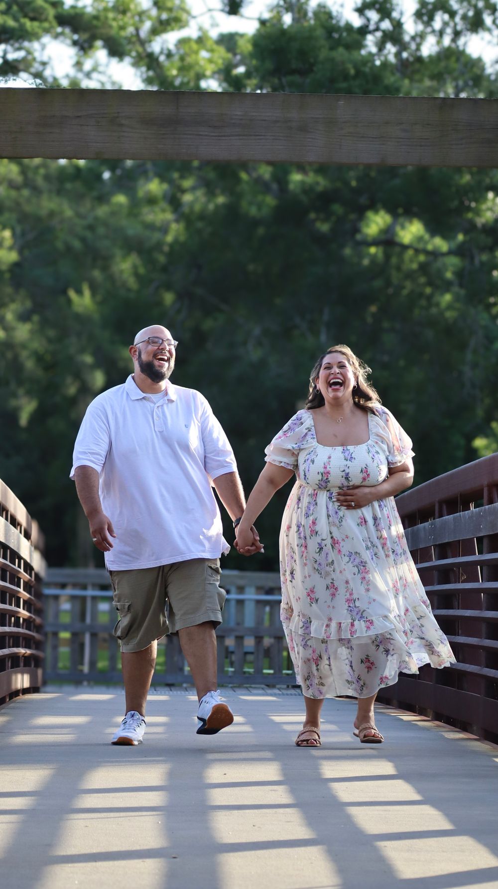 Playful couple in white outfits laughs together on wooden bridge.