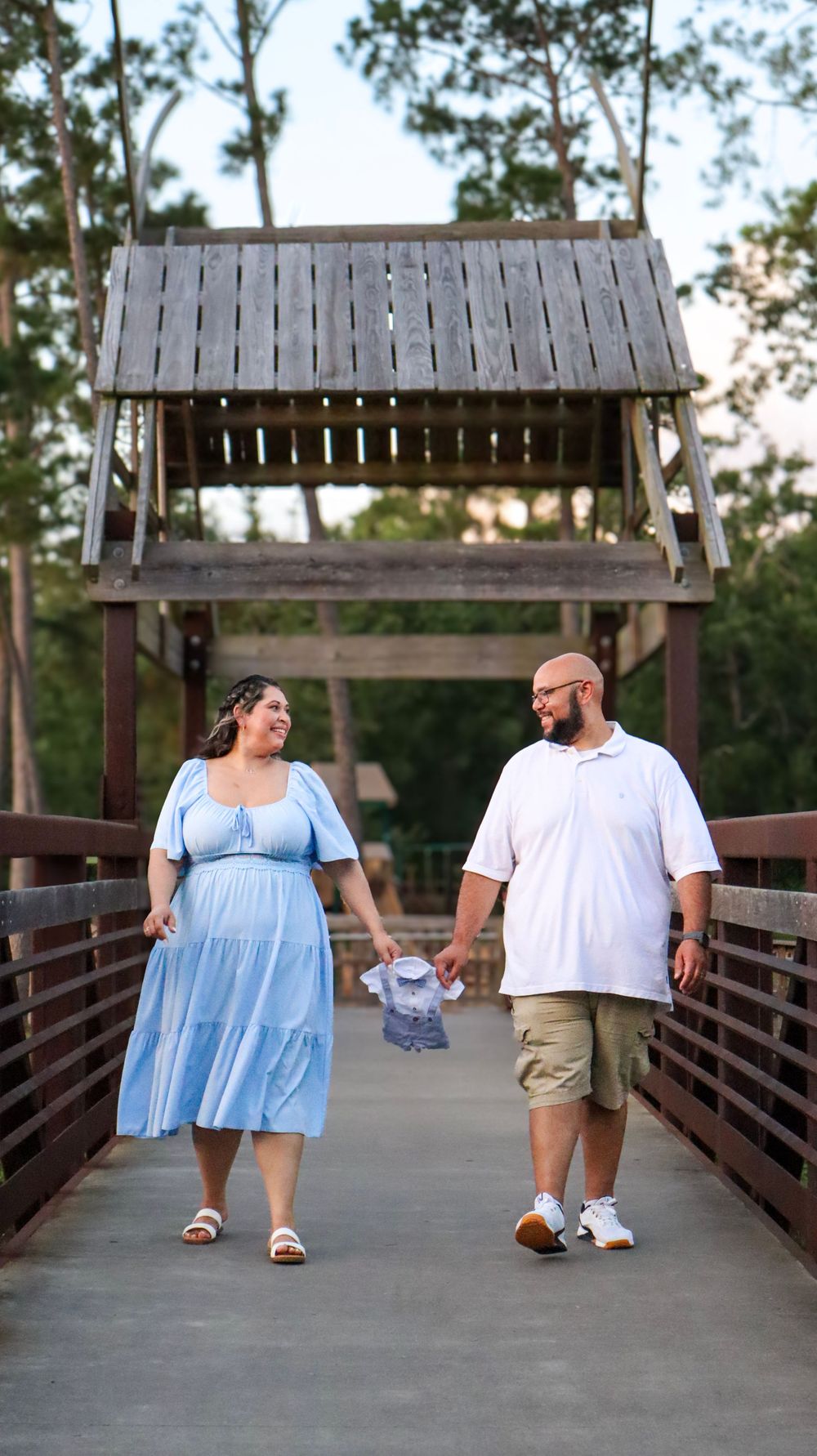 A couple walks together on a wooden covered bridge in a park during sunset.