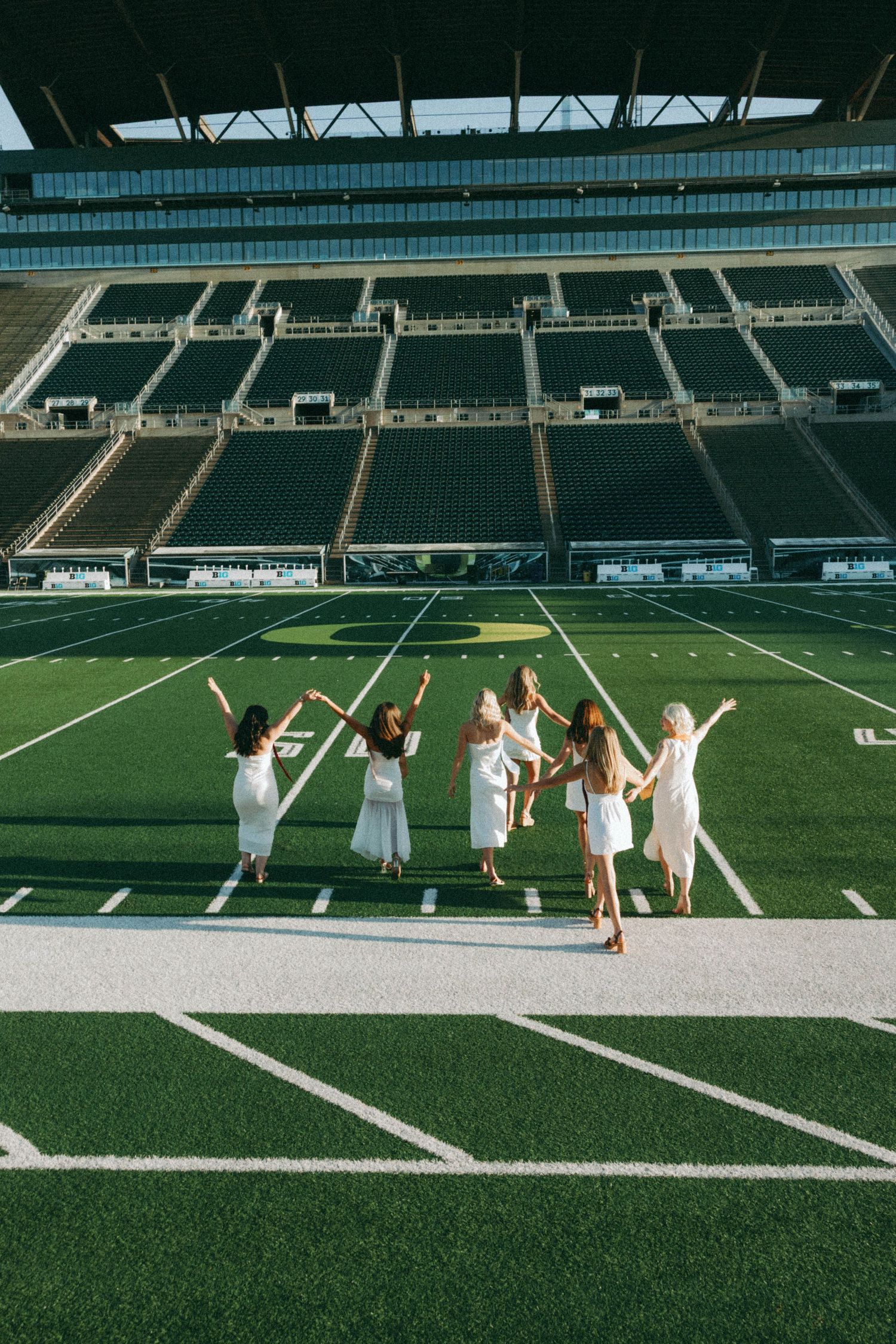 A photoshoot in a golden field with Autzen Stadium visible in the background on a sunny afternoon.