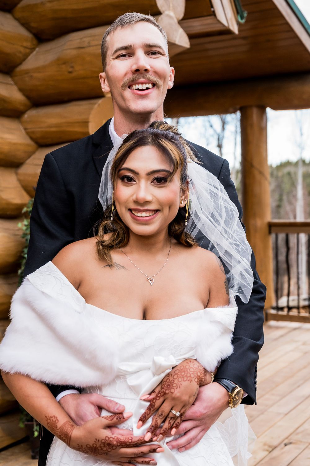 A happy newlywed couple embraces on a rustic wooden cabin porch during their winter wedding celebration.
