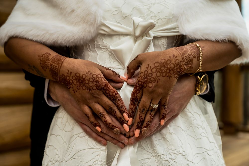 Close-up detail shots of hands adorned with intricate henna designs and wedding jewelry against white fabric.