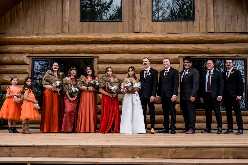 Wedding party members stand in formal attire on rustic wooden steps at an outdoor venue.