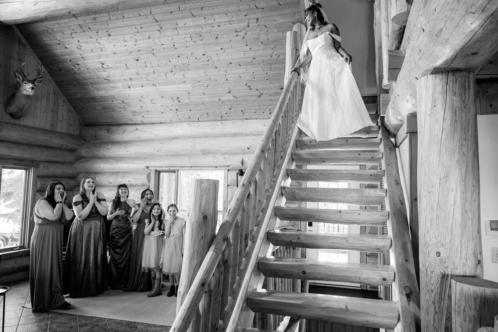 A black and white photo of a person in a wedding dress standing on rustic wooden stairs.