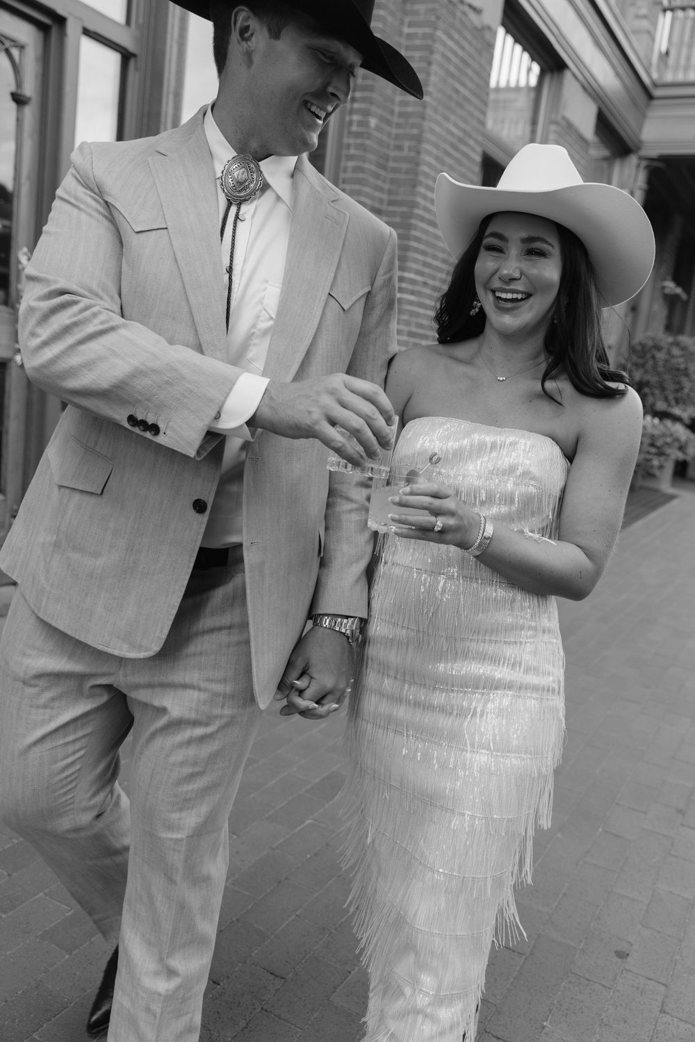 A couple in matching light colored outfits embraces and laughs together in a series of candid black and white photos.