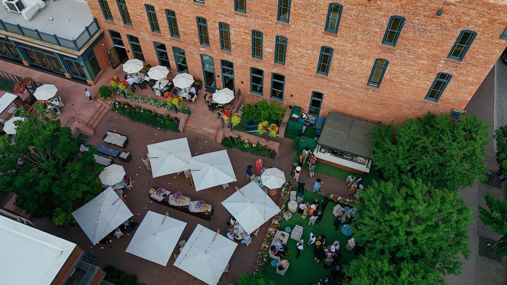 Aerial view of a rooftop garden with tables, chairs and greenery on top of a brick building in an urban setting. aspen colorado