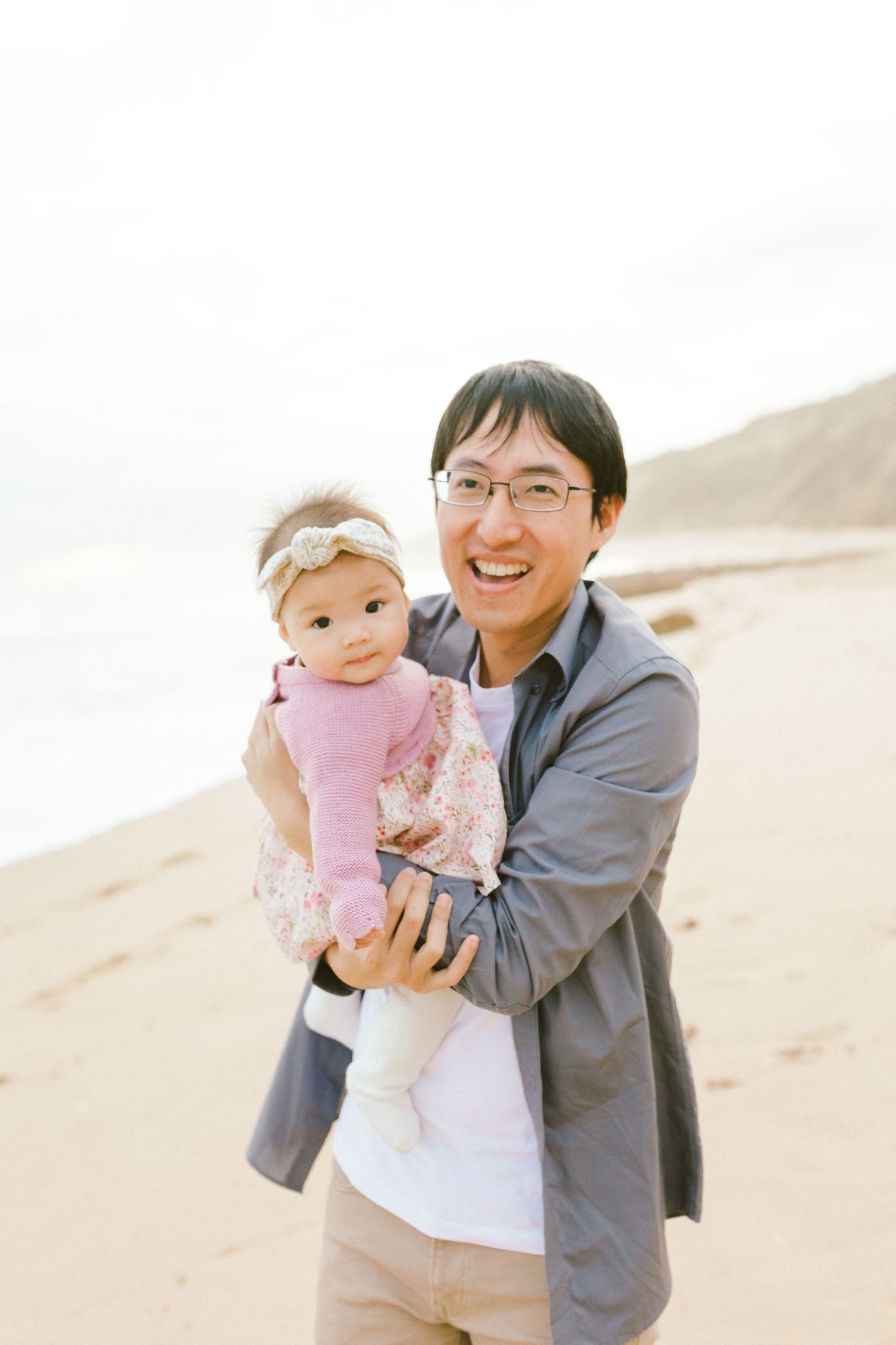 Sweet family portraits captured on a sandy beach showing joyful moments between parent and baby in pink.