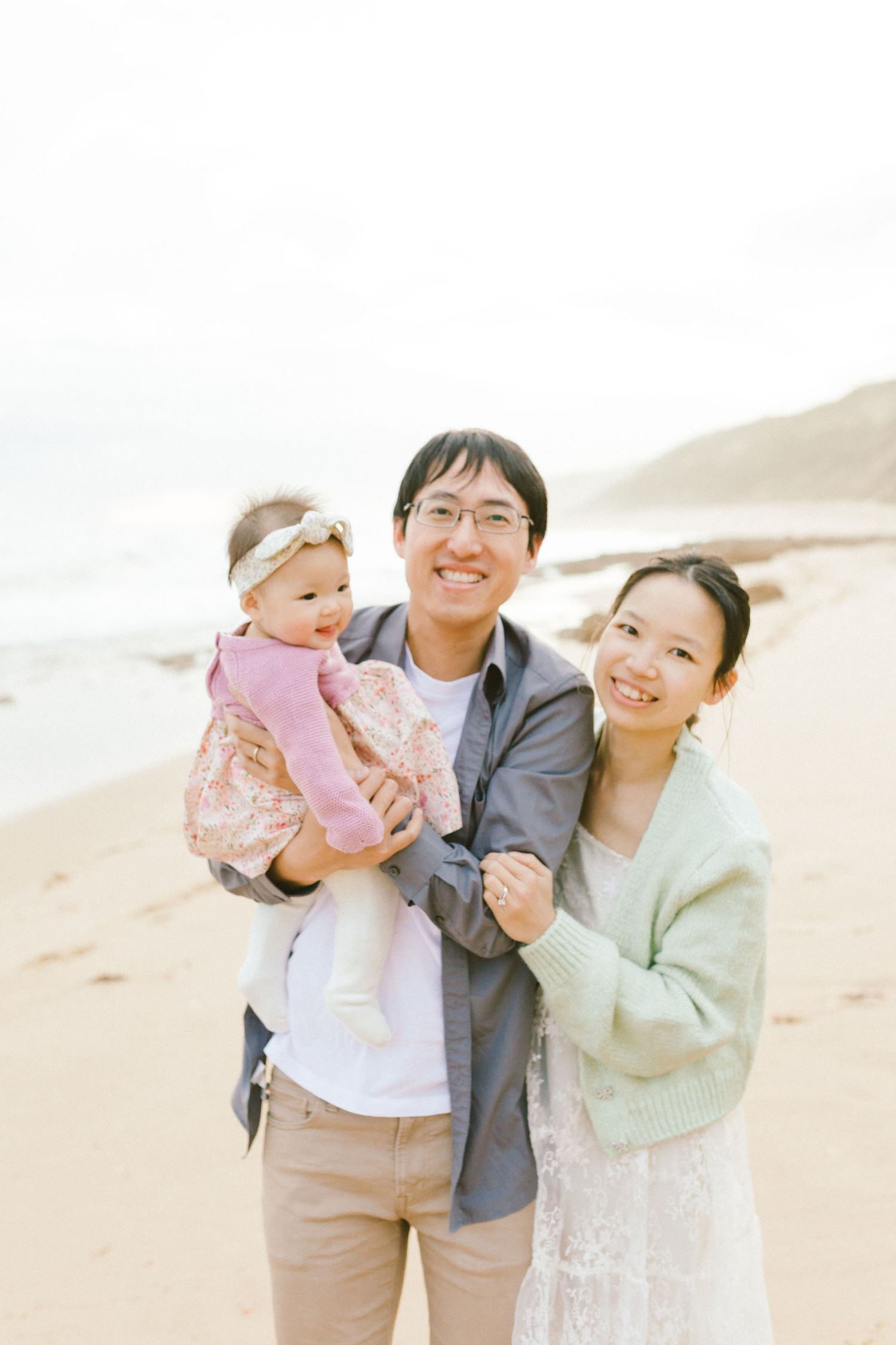 A happy family poses together on a sandy beach during golden hour.