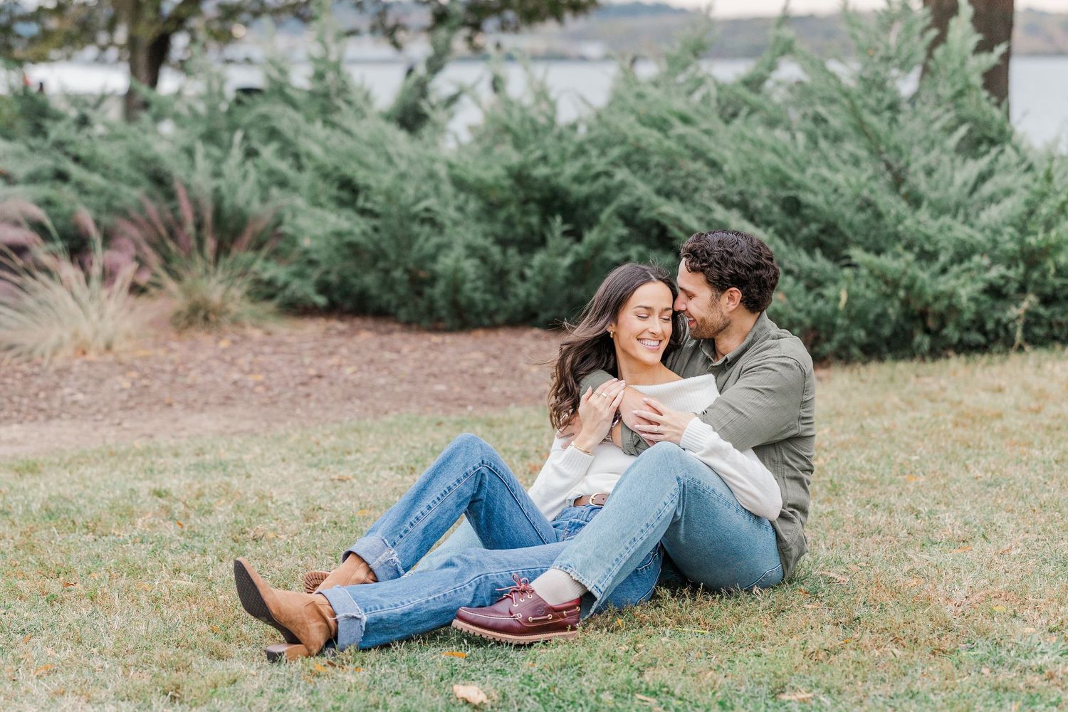 A couple in casual denim outfits lies together on green grass during an outdoor photo session.