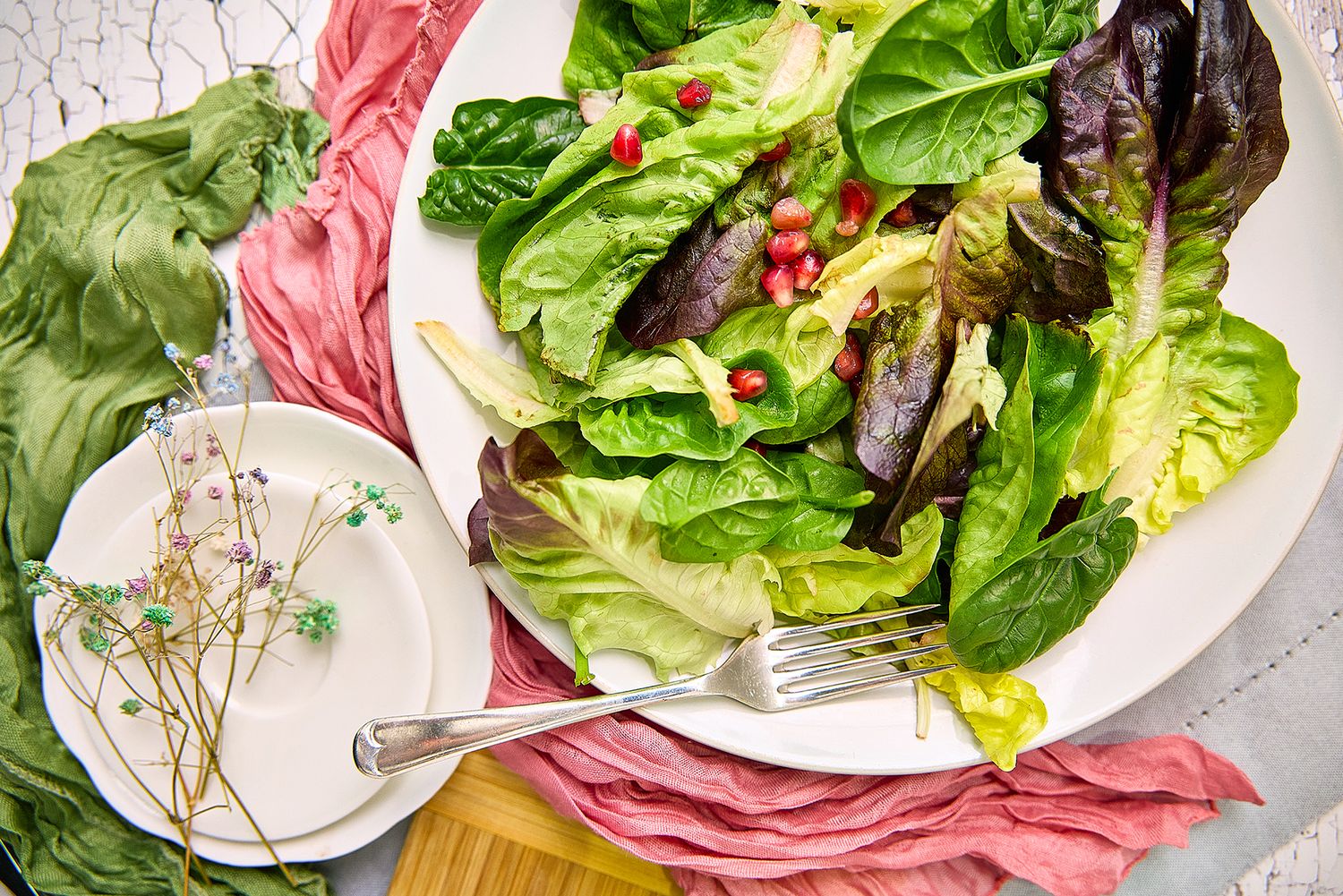 Food Flatley of a vibrant bed of salad leaves with side white plate styled with flowers and fabric shot by Helen Yandell Photography