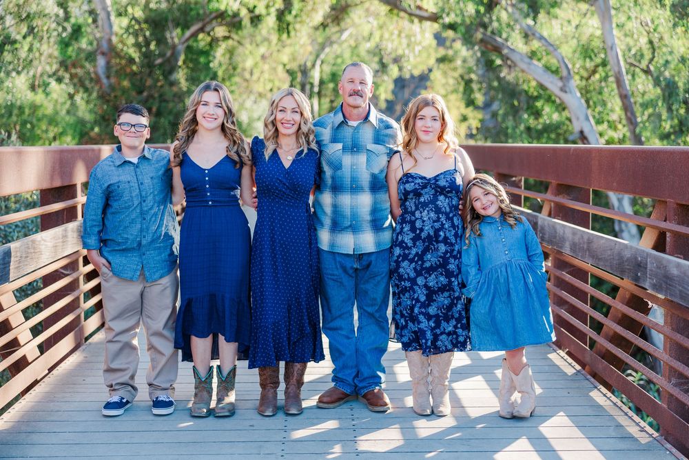A group wearing coordinated navy blue outfits poses together on a wooden bridge in a natural setting.